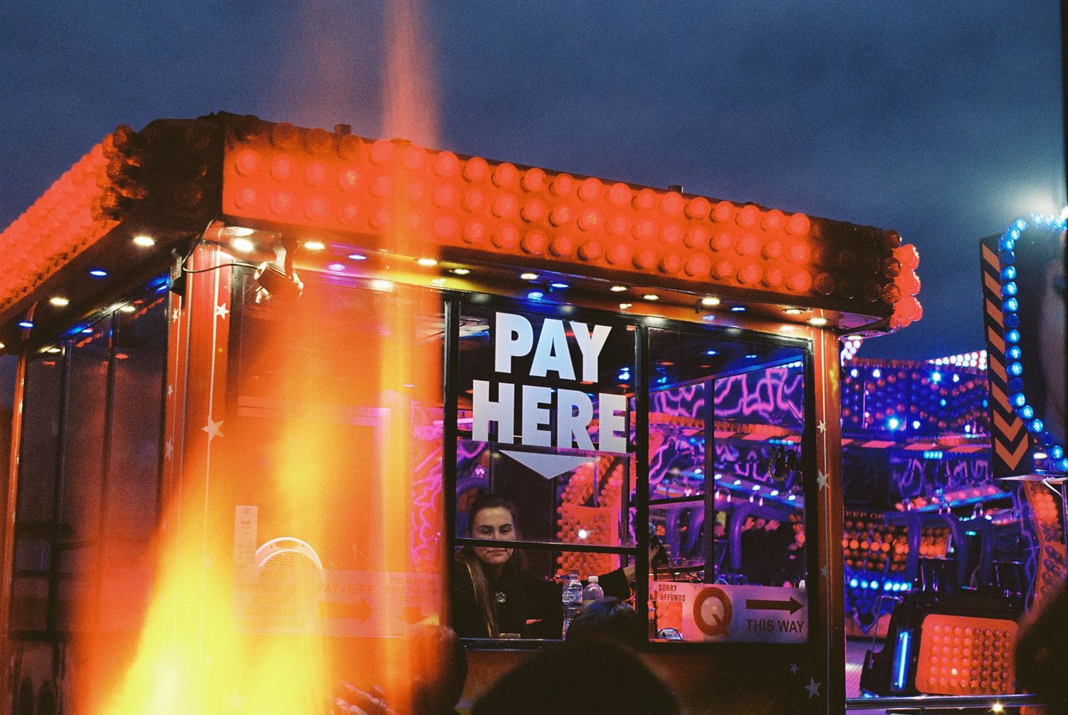 Colorful neon signs illuminate a nighttime bar or restaurant exterior with glowing red and blue lighting.