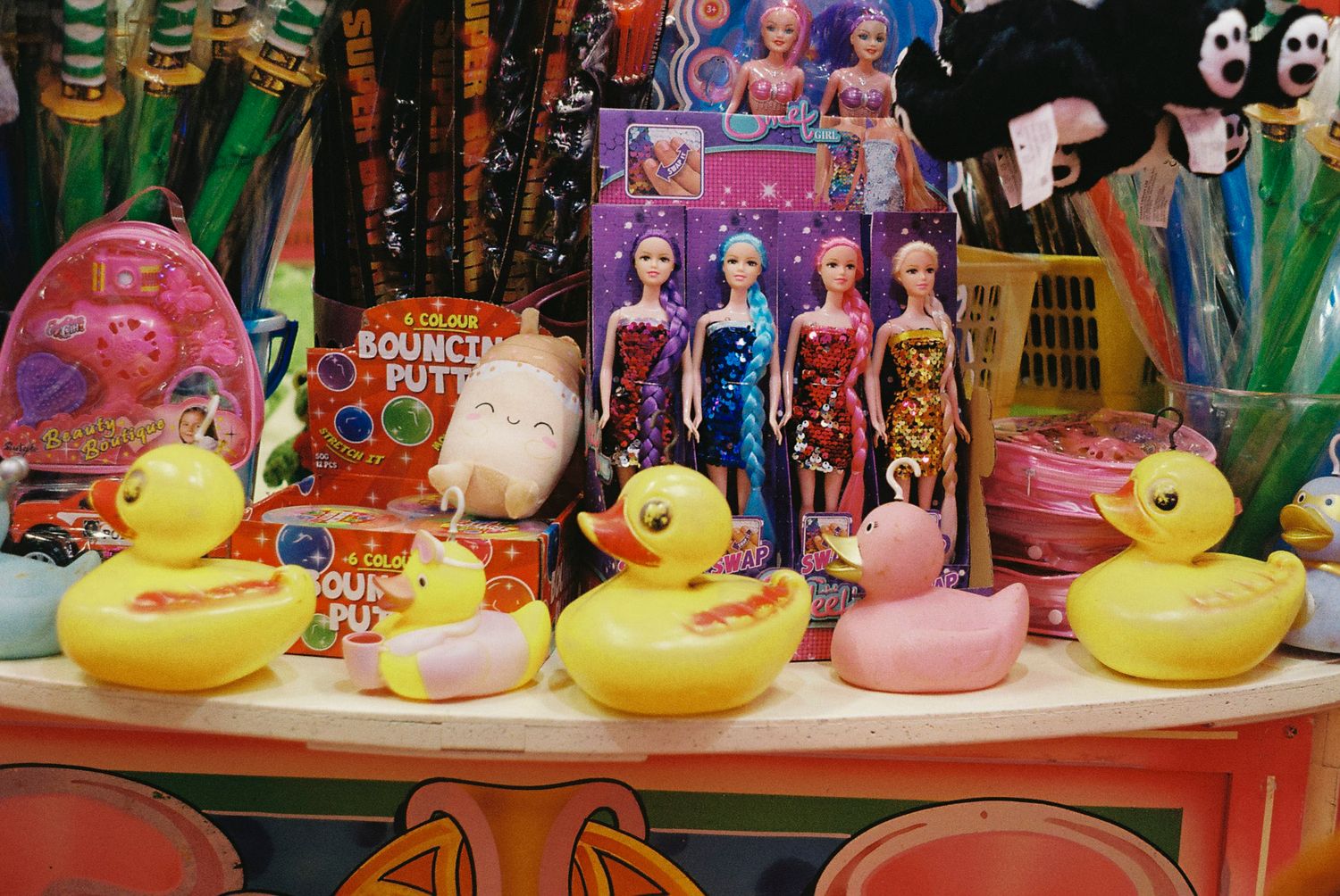 Colorful rubber ducks lined up on a shelf in a toy store display with other plush toys and merchandise.
