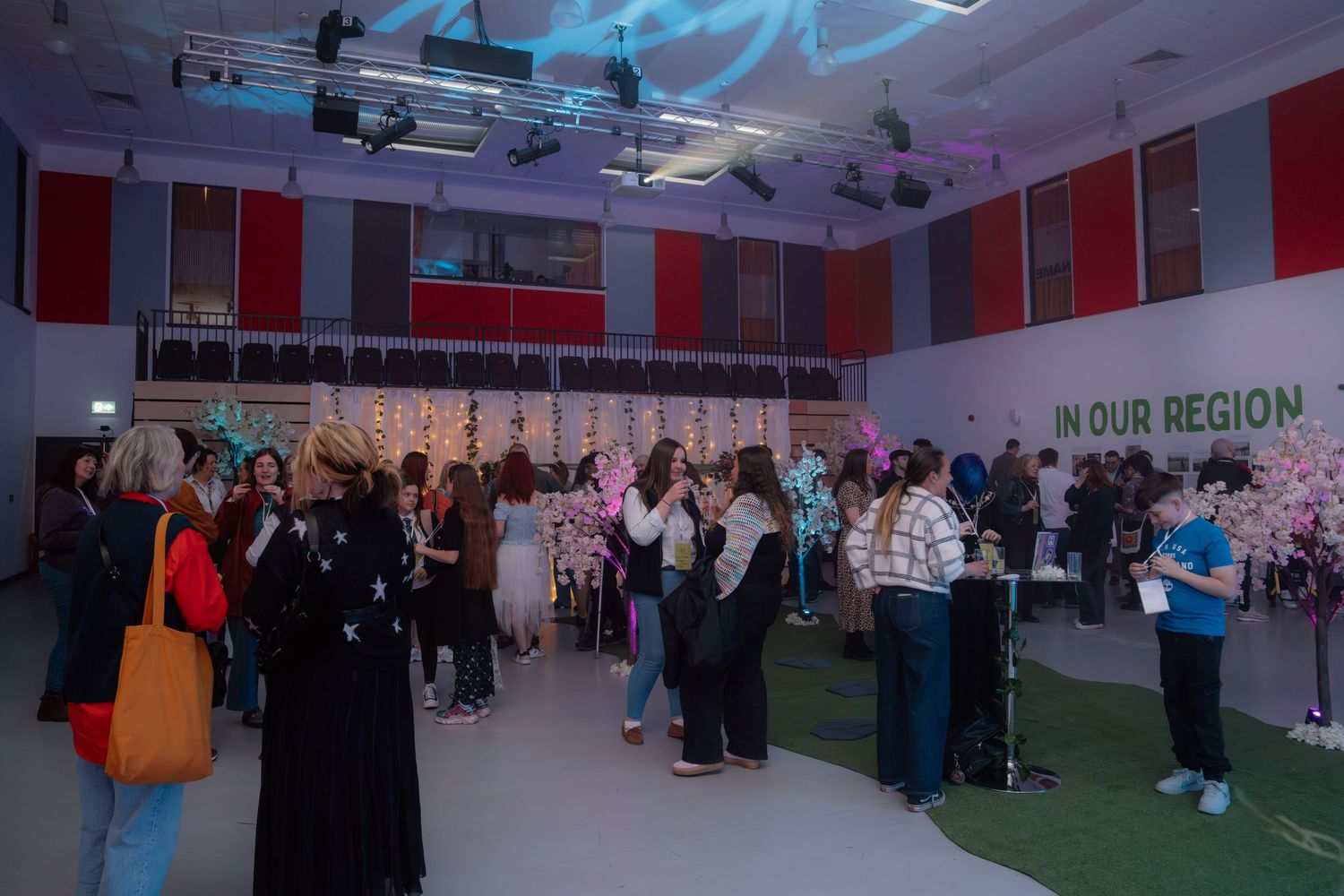 People networking at an indoor regional event with floral displays and 'In Our Region' signage.