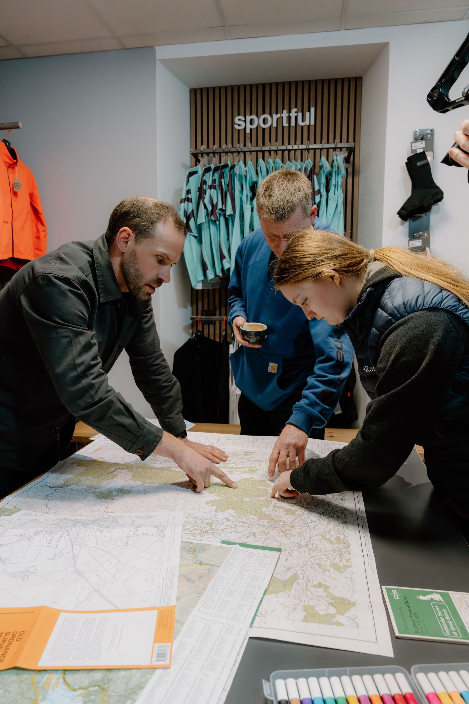 Three people study a detailed map on a table inside a Sportful cycling apparel store, planning a route together.