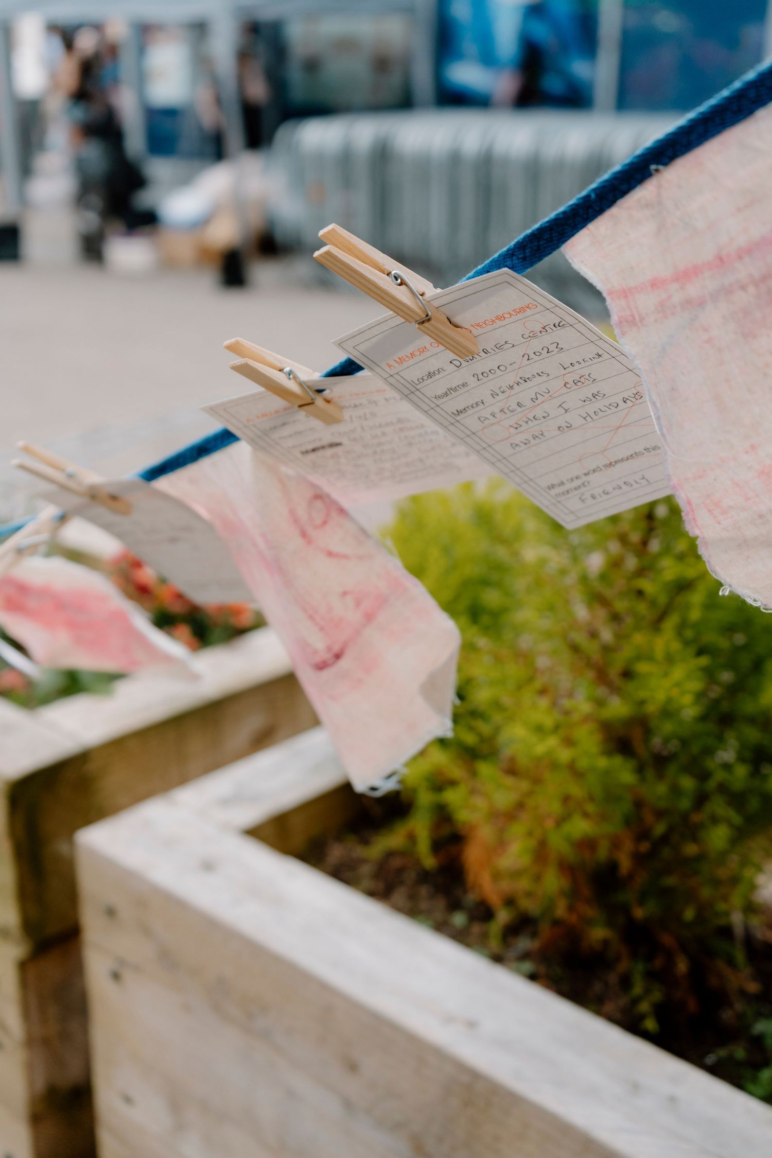 Handwritten notes clipped with wooden clothespins to a string above wooden planter boxes outdoors.