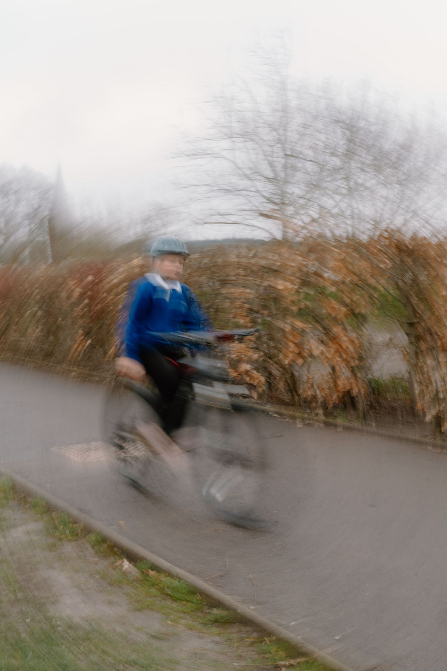 Blurred motion photo of an elderly man riding a bicycle on a path surrounded by autumn trees.