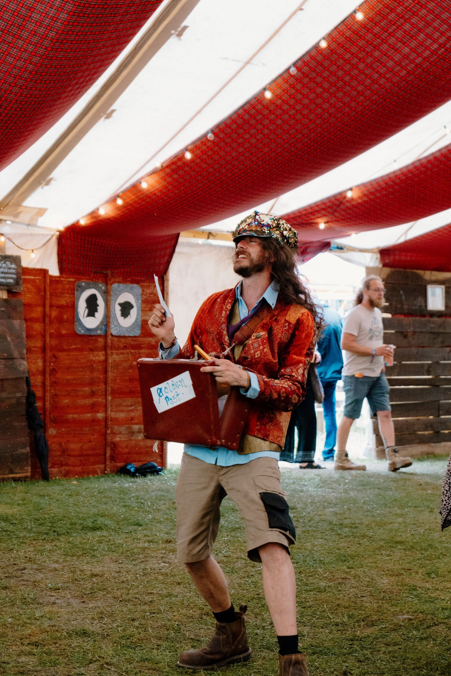 People gather under a red and white striped tent at an outdoor festival or event.