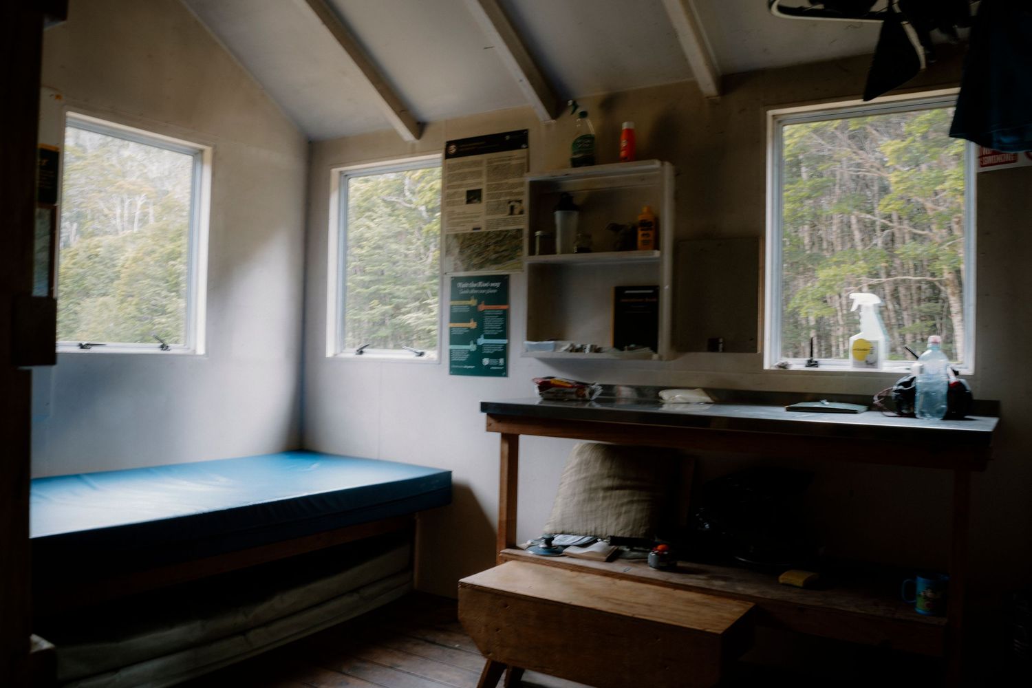 Interior view of a rustic cabin with multiple windows and wooden walls showing natural lighting throughout the space.