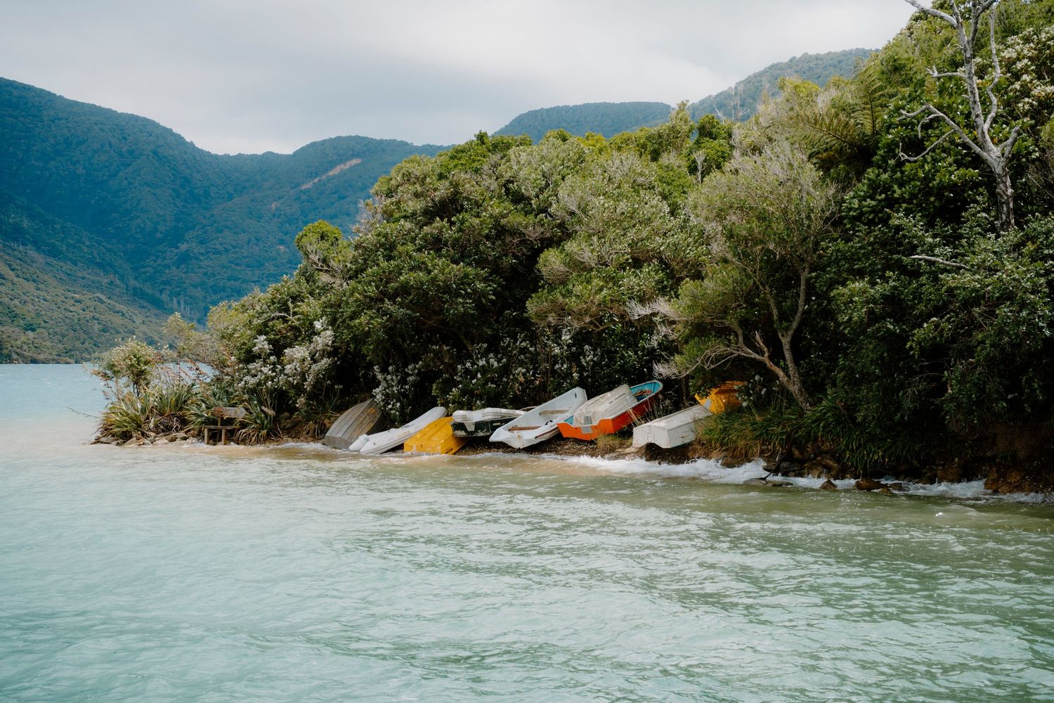 Scenic mountain lake surrounded by lush green forests with colorful kayaks lined up along the rocky shoreline.