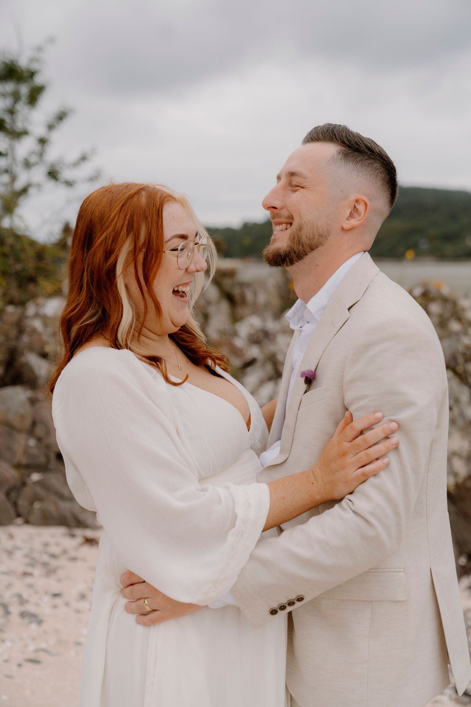A couple in white outfits share joyful candid moments during their beach wedding photo session.