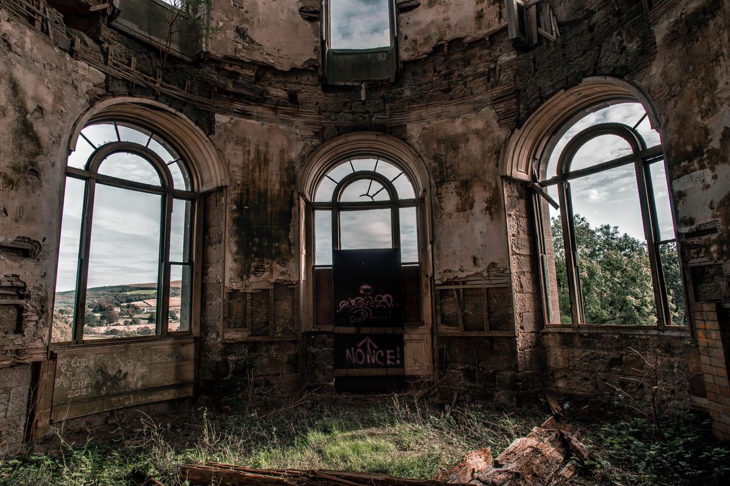 Interior view of an abandoned circular building with arched windows and crumbling walls showing signs of decay and neglect.