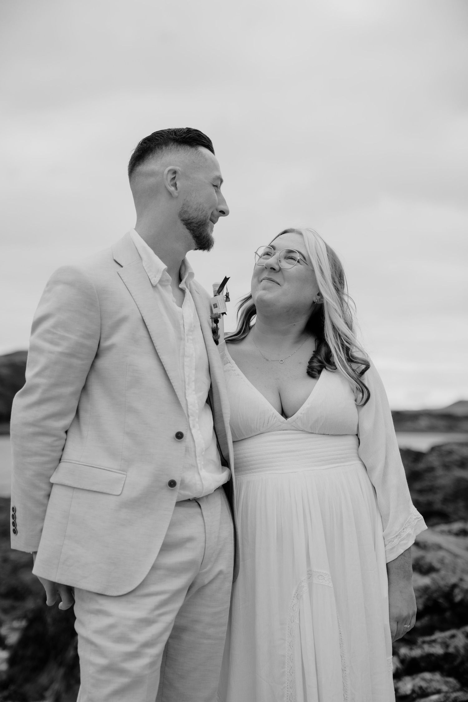 Black and white wedding portrait showing couple in elegant attire against cloudy sky.