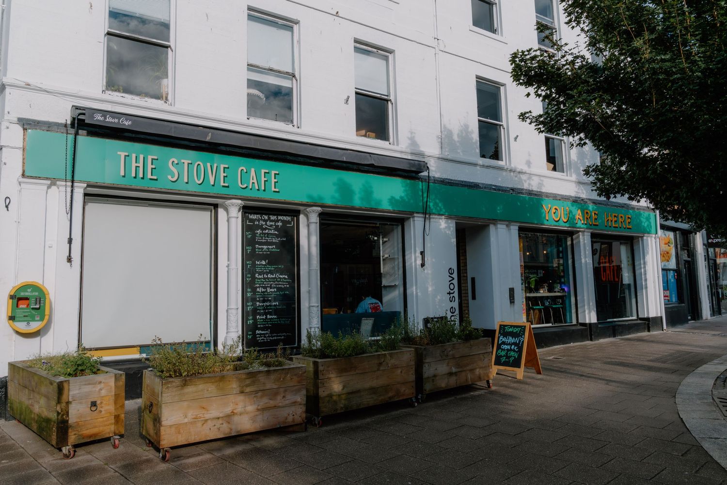 The Stove Cafe exterior with green awning, wooden planters, and chalkboard signs on a quiet street.