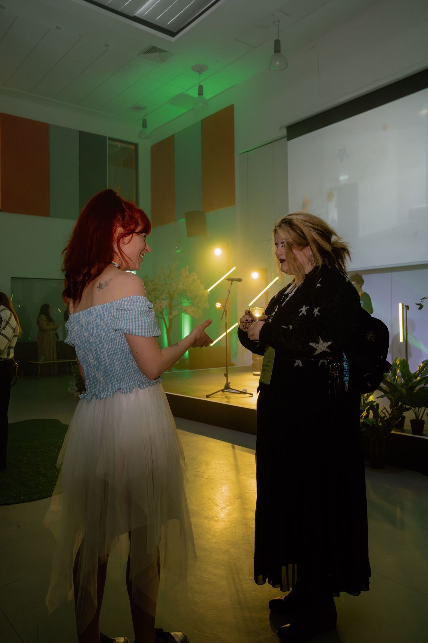 Two women dancing at an indoor event, one in a blue off-shoulder dress, the other in a black star-print outfit.