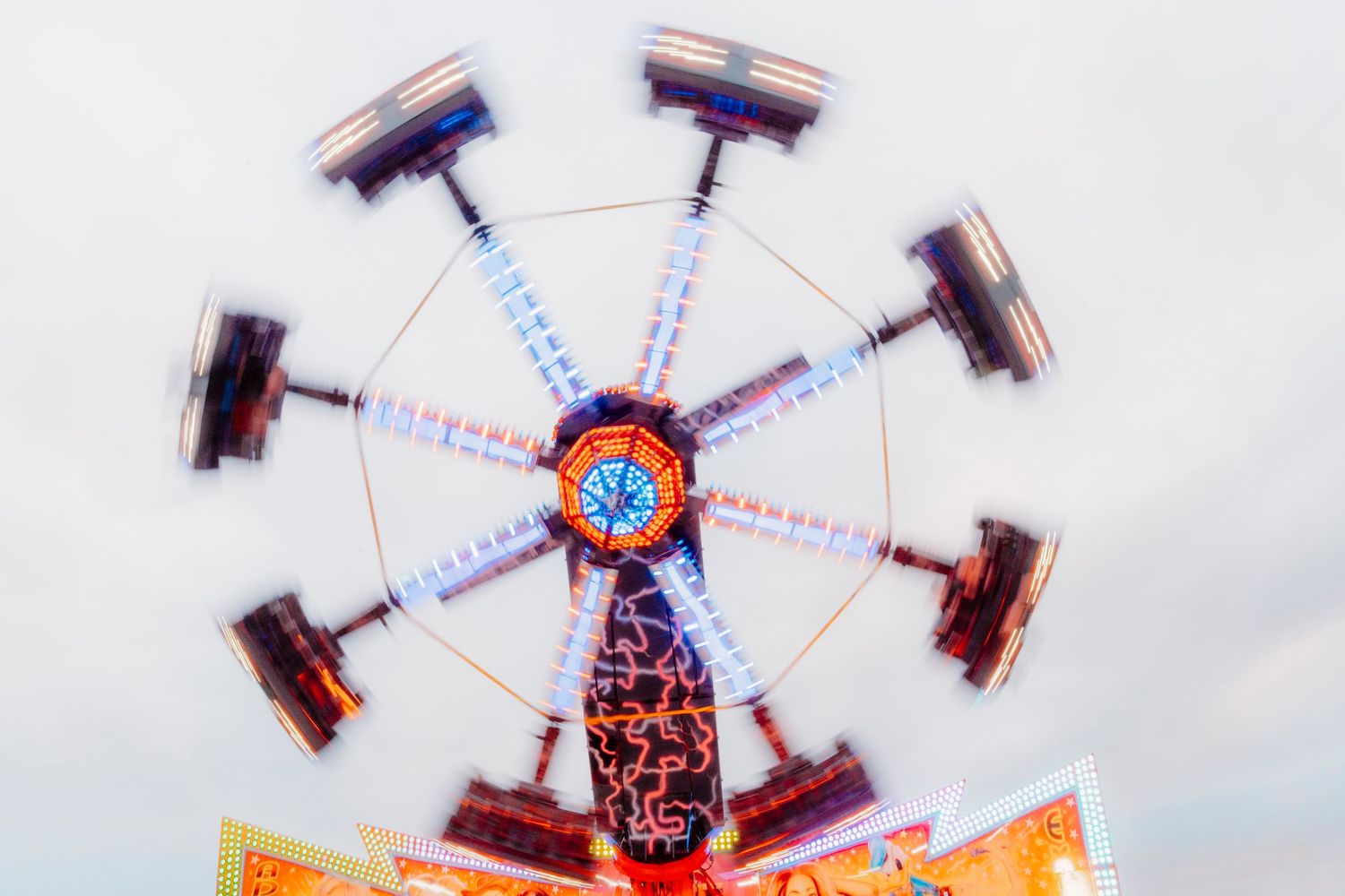 Multiple exposure photo sequence showing a carnival ride spinning in a circular motion against a light sky background.
