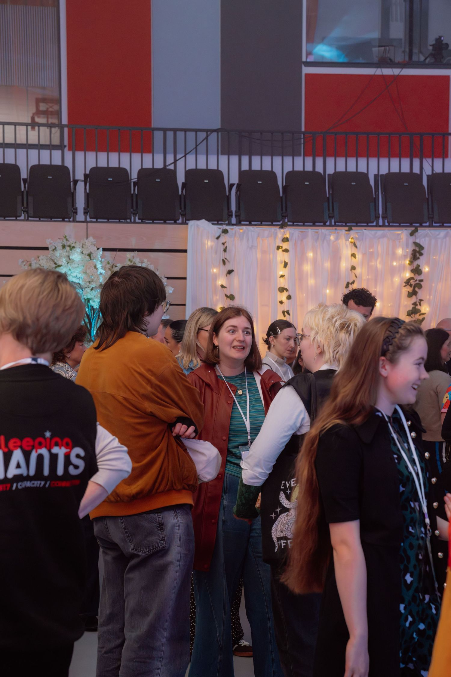 Young people mingling at an indoor event with fairy lights backdrop and empty theater seats.