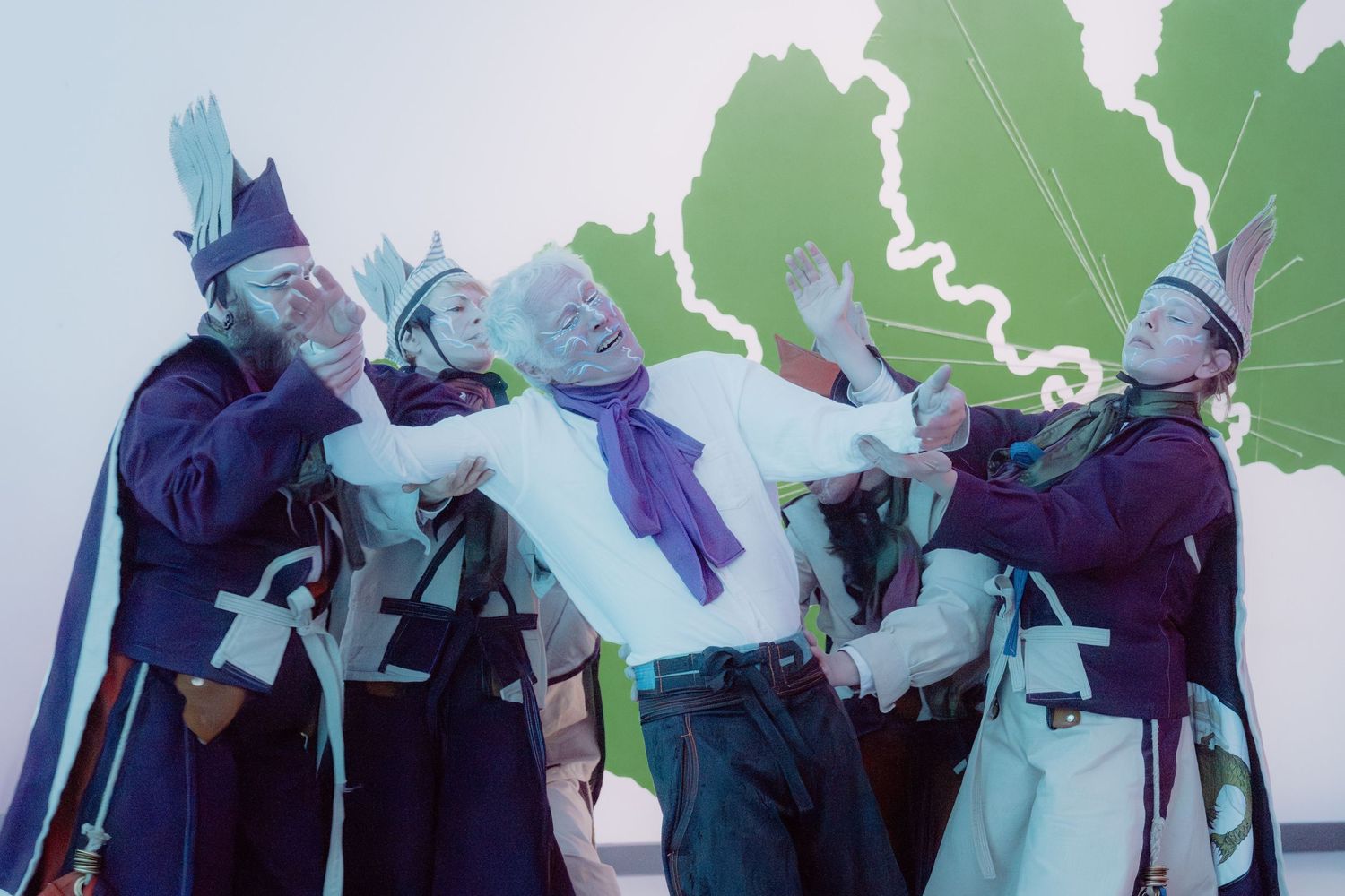 People in colorful historical costumes pose dramatically in front of a green map backdrop.