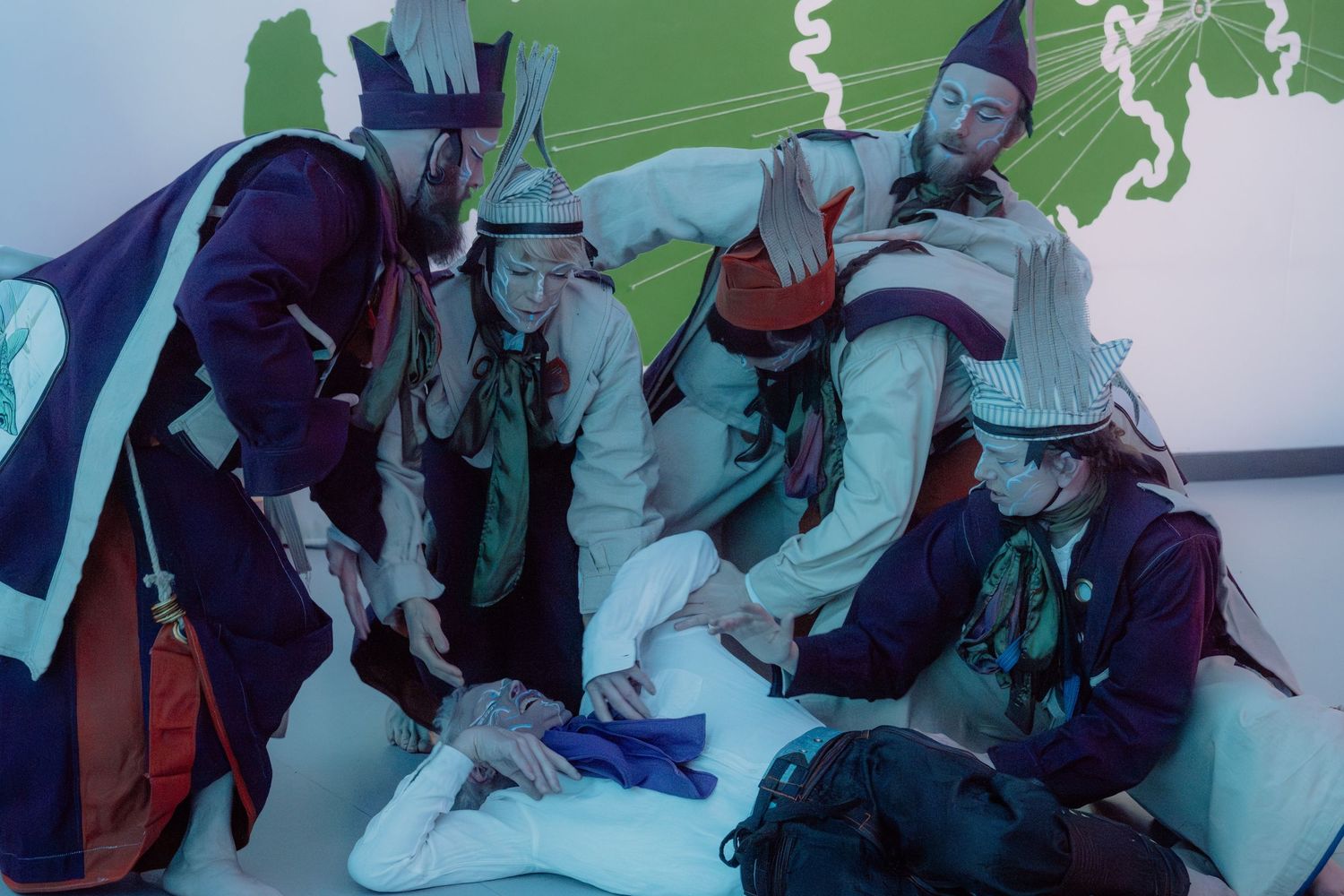 Group of people in colorful costumes and pointed hats gathered around a figure in white indoors.