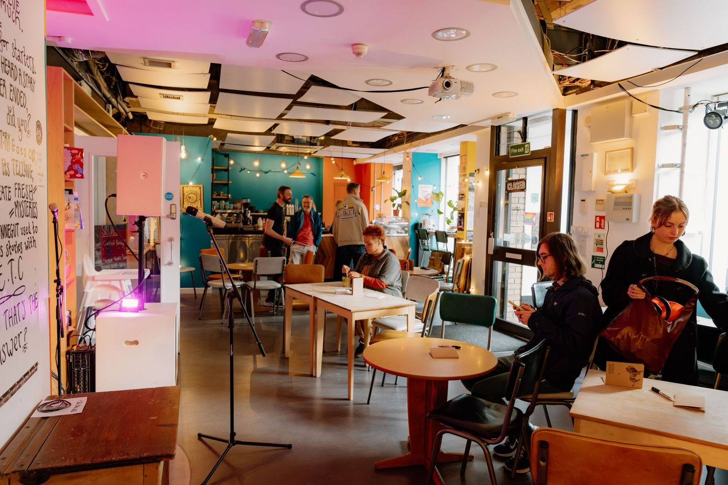 Vibrant coworking space with people collaborating, colorful decor, wooden tables, and pink lighting accents.
