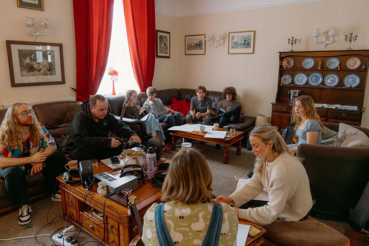 Group of people gathered in a cozy living room for a meeting, sitting on sofas surrounded by vintage decor and blue plates.