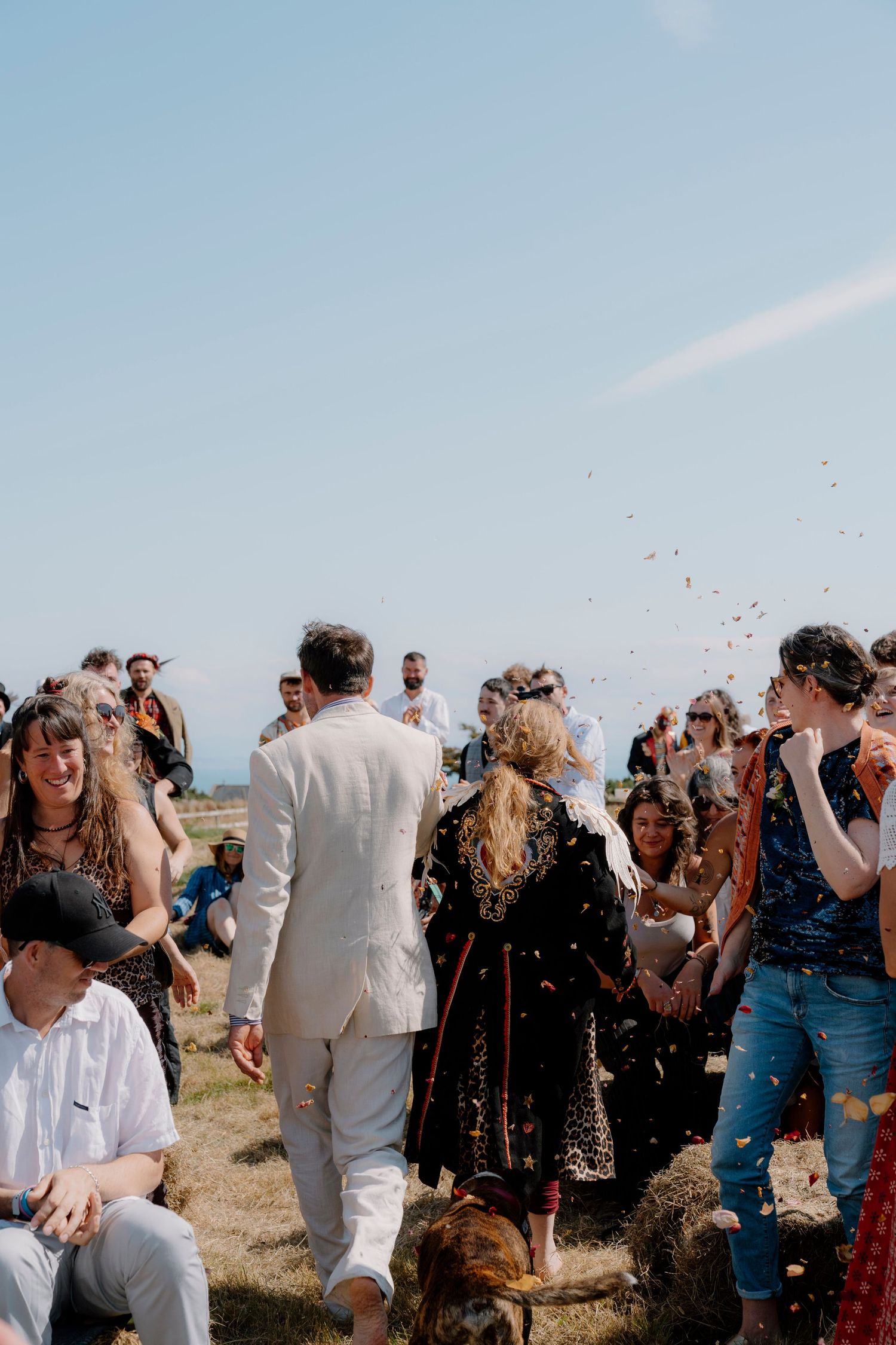 A group of people celebrate outdoors on a sunny day with confetti in the air during a festive gathering.
