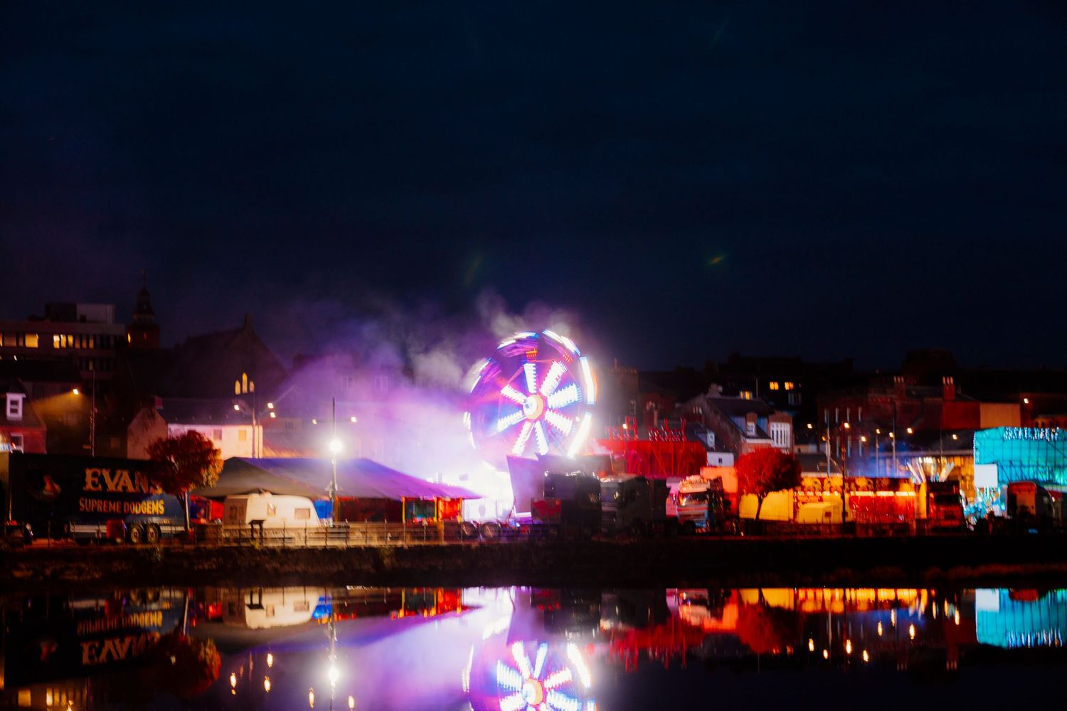 A colorful nighttime carnival scene with glowing rides and attractions creating a vibrant atmosphere against the dark sky.
