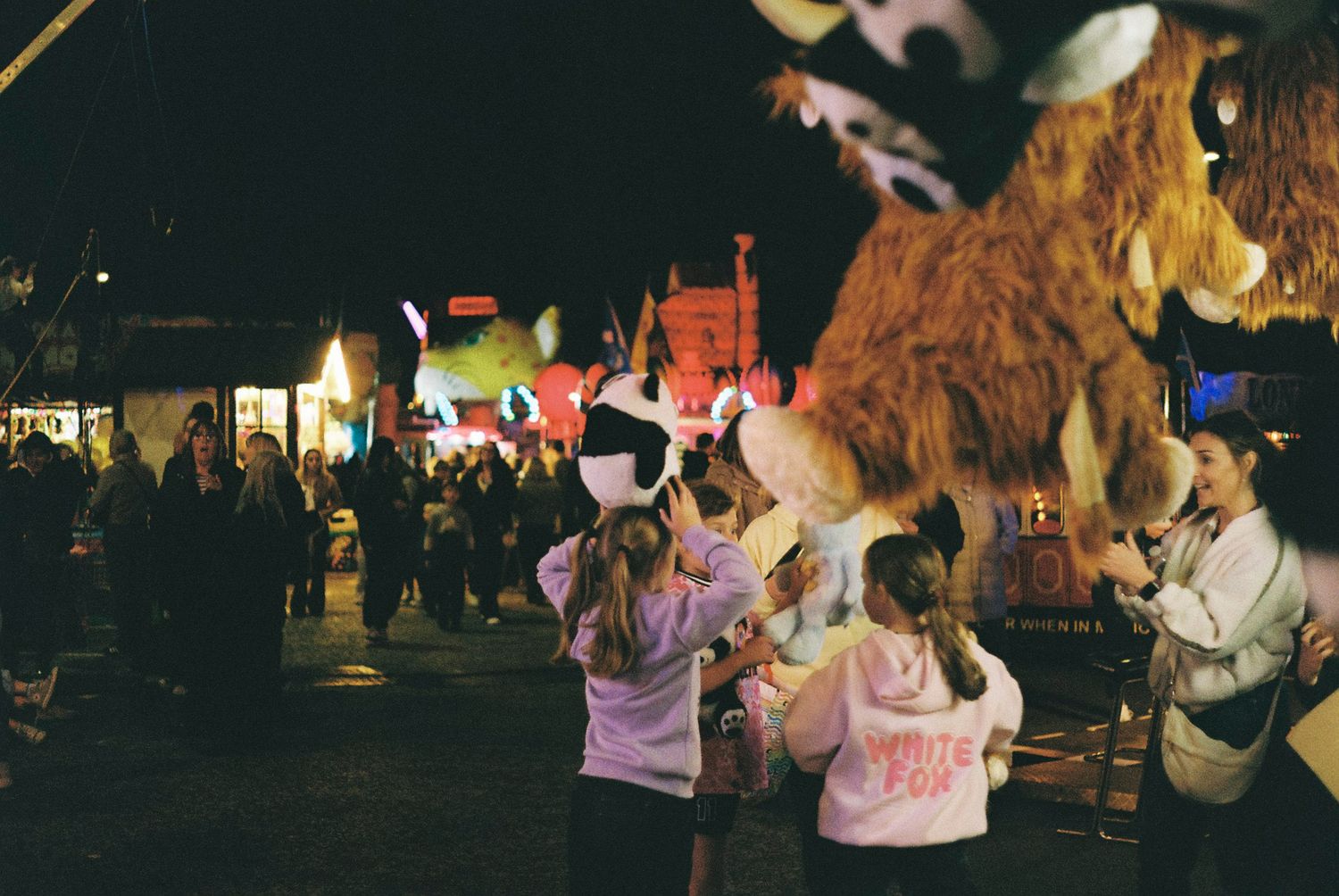 People dance and celebrate at an outdoor festival with glowing lights and decorations in the evening.