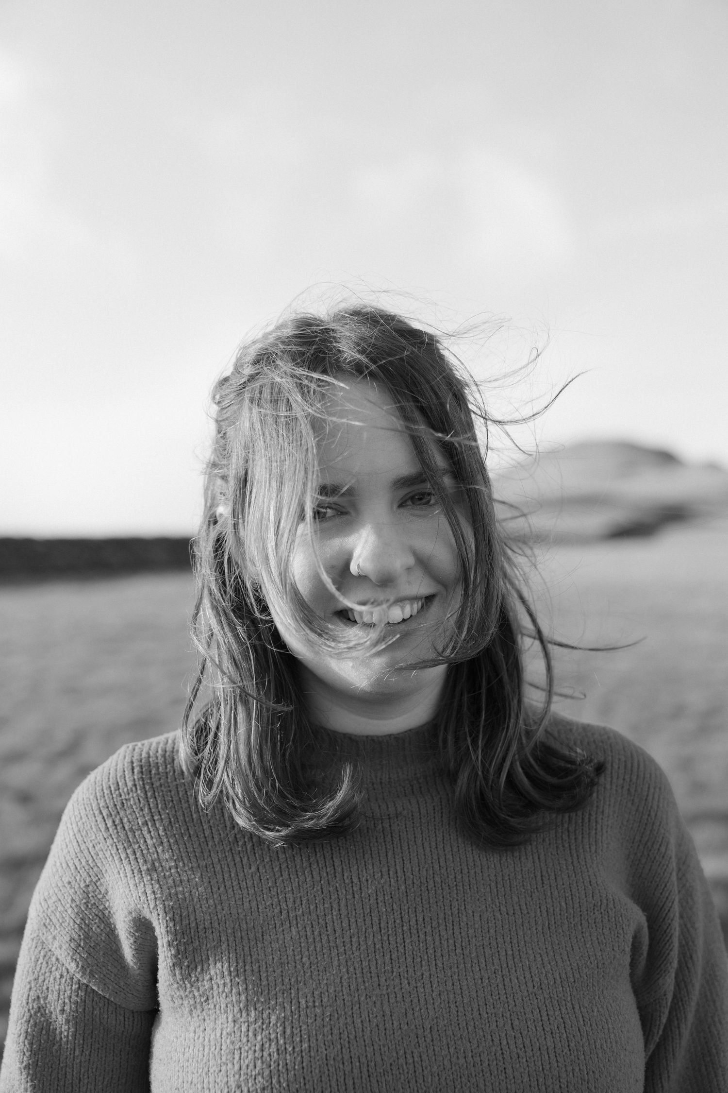 A sequence of black and white portraits showing a person with windswept hair wearing a knit sweater outdoors.