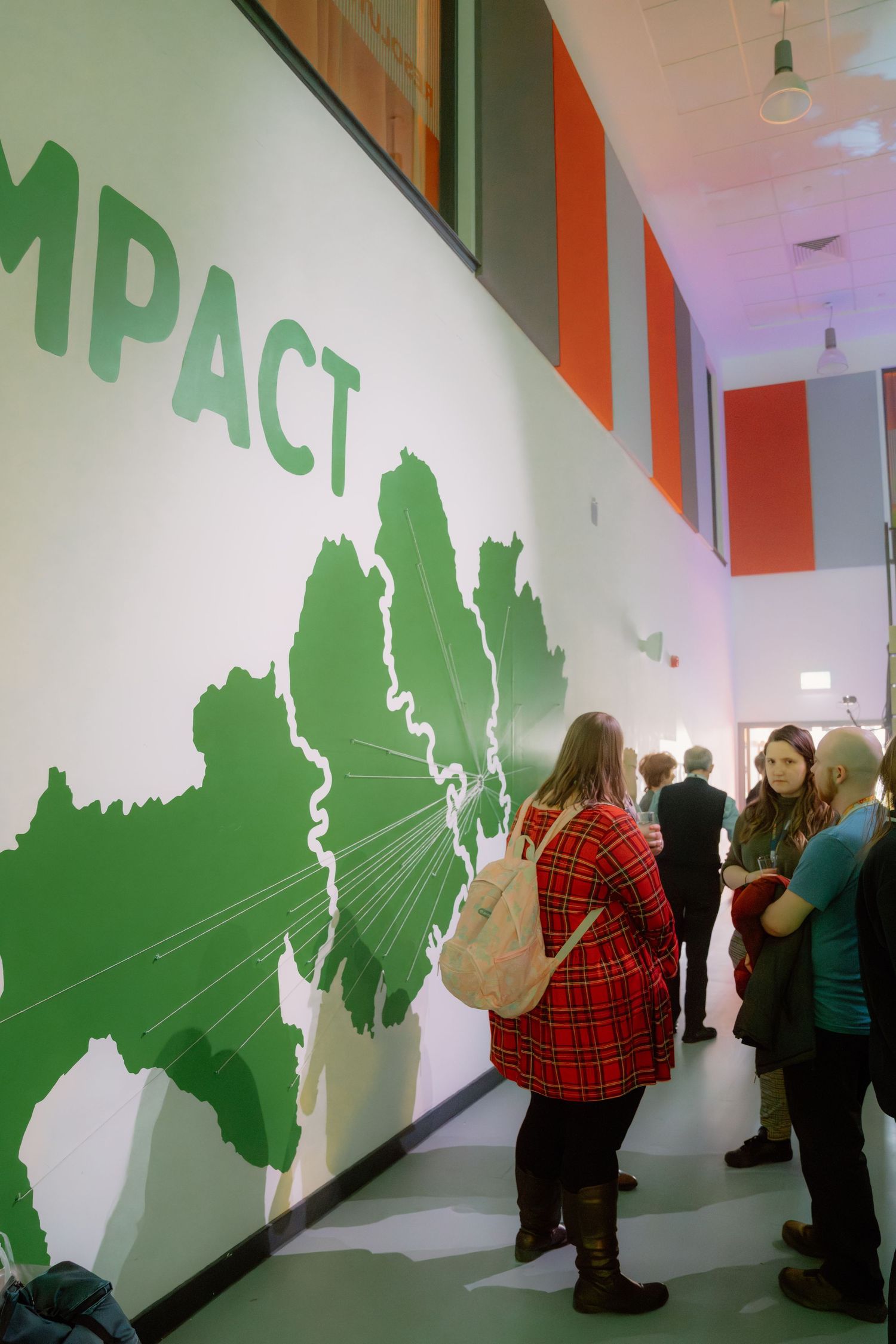 People viewing a large green world map mural with IMPACT text in a modern corridor.
