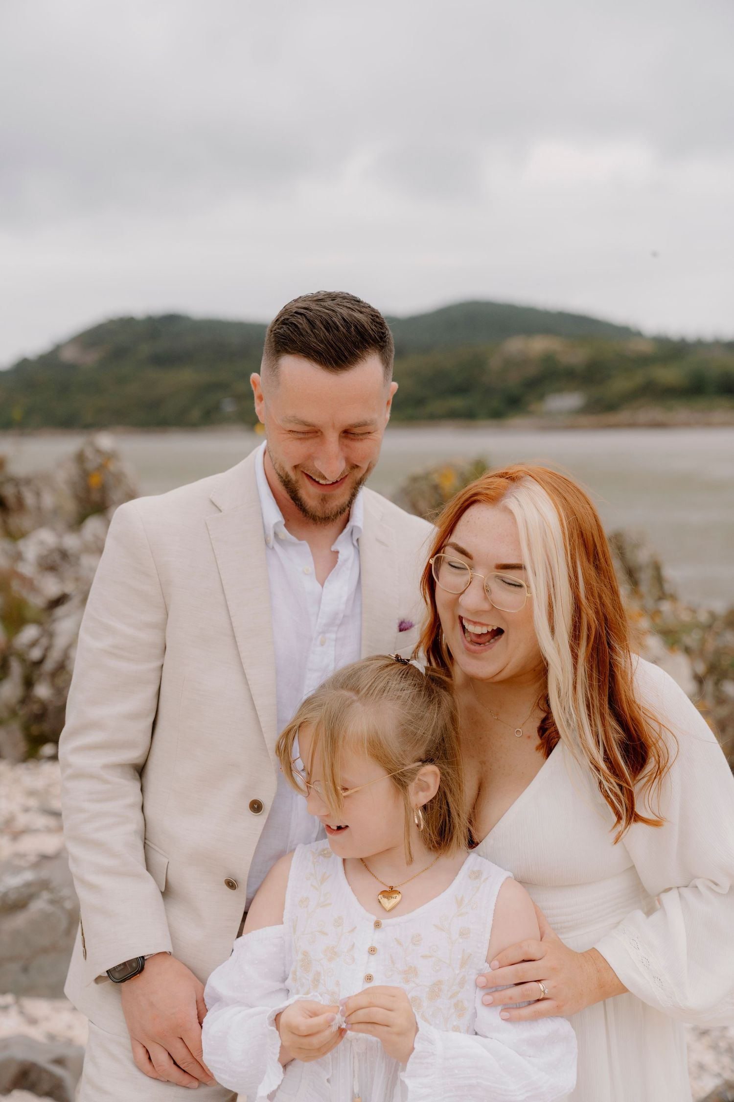 A joyful family moment captured on a rocky beach with everyone wearing light colored clothing.