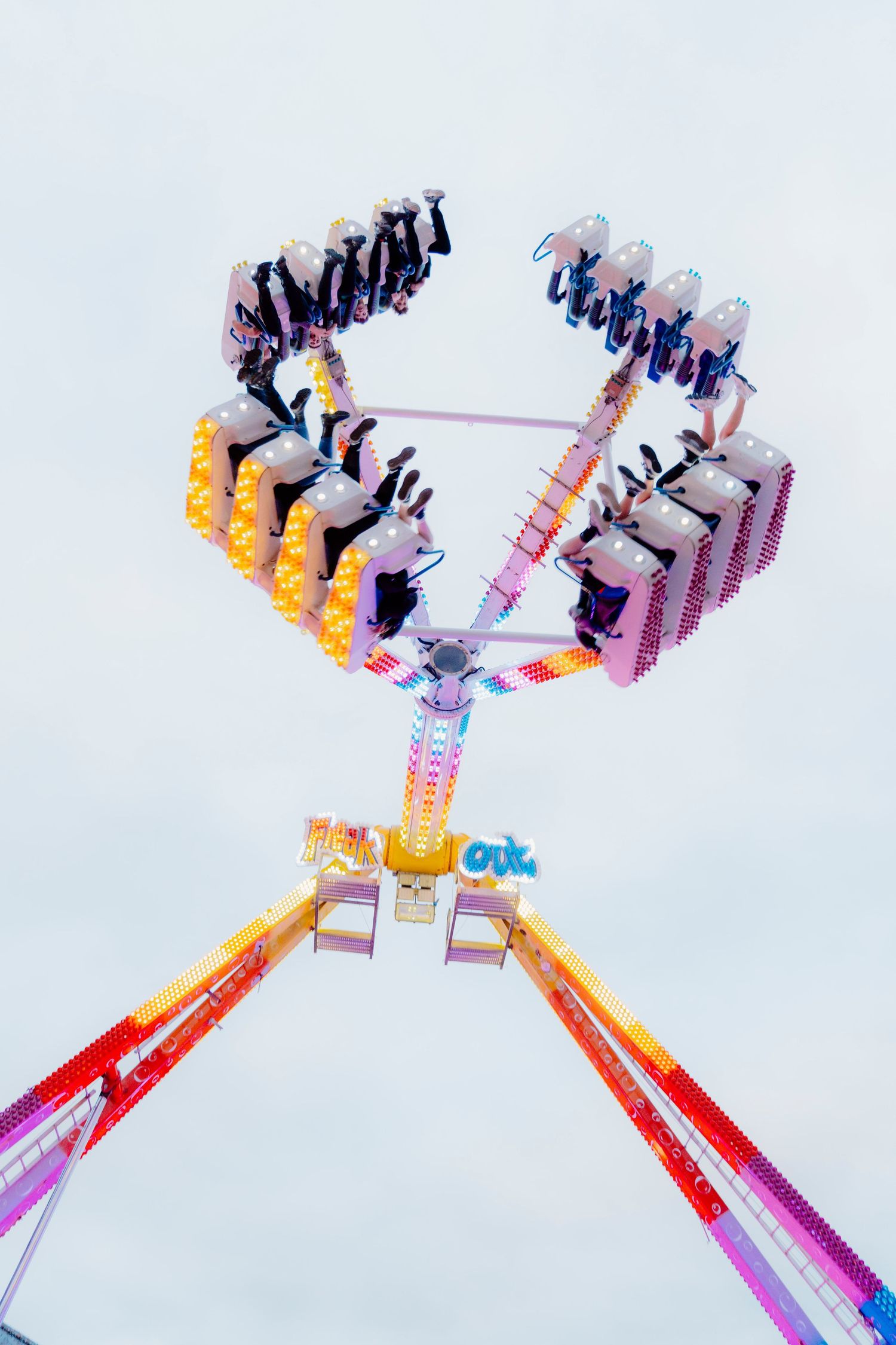 Carnival ride spinning in motion against white sky showing multiple seats and mechanical arms in vibrant red and yellow colors.