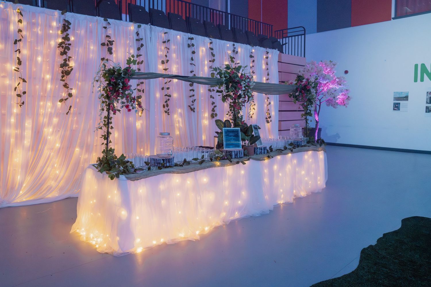 Elegant wedding reception table with fairy lights, floral greenery, and a glowing backdrop in a decorated event venue.