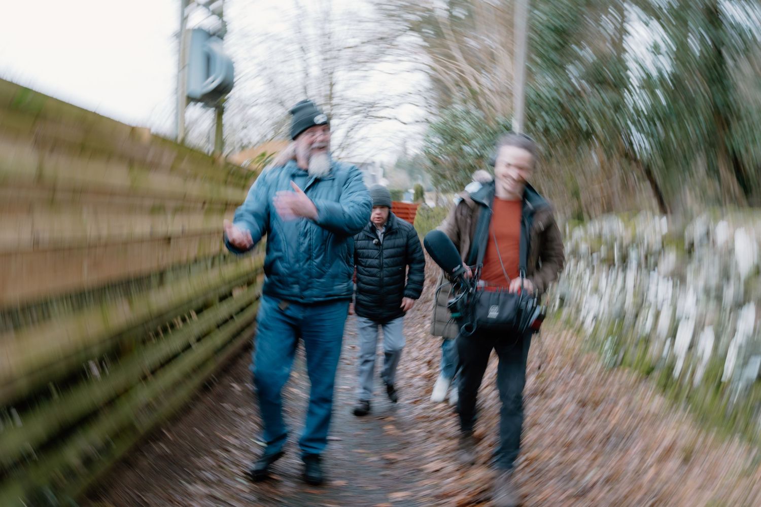 Three men walking along a moss-covered path through a wooded area on an overcast day.