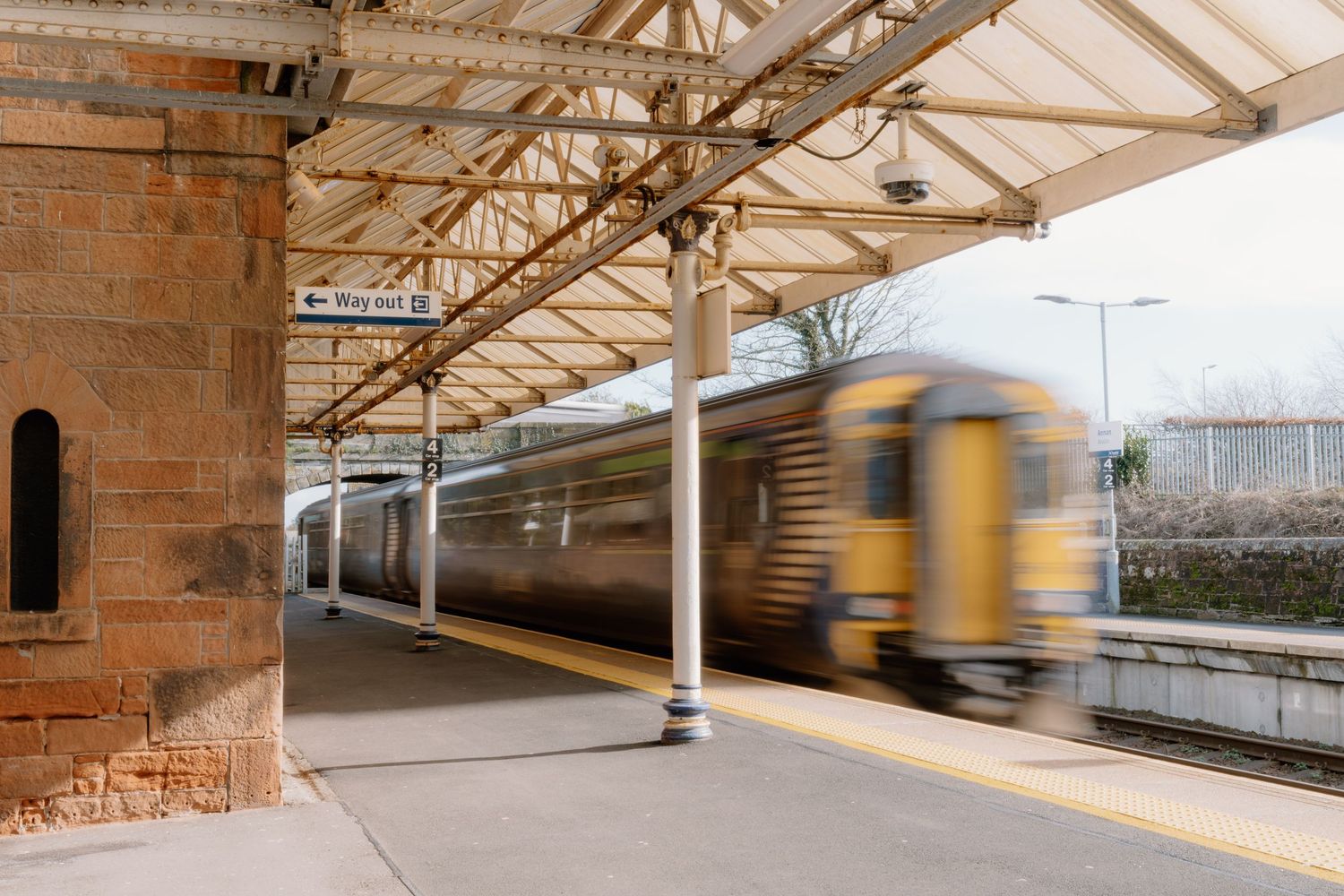 A yellow and brown train speeding through a covered UK railway station platform with motion blur effect.