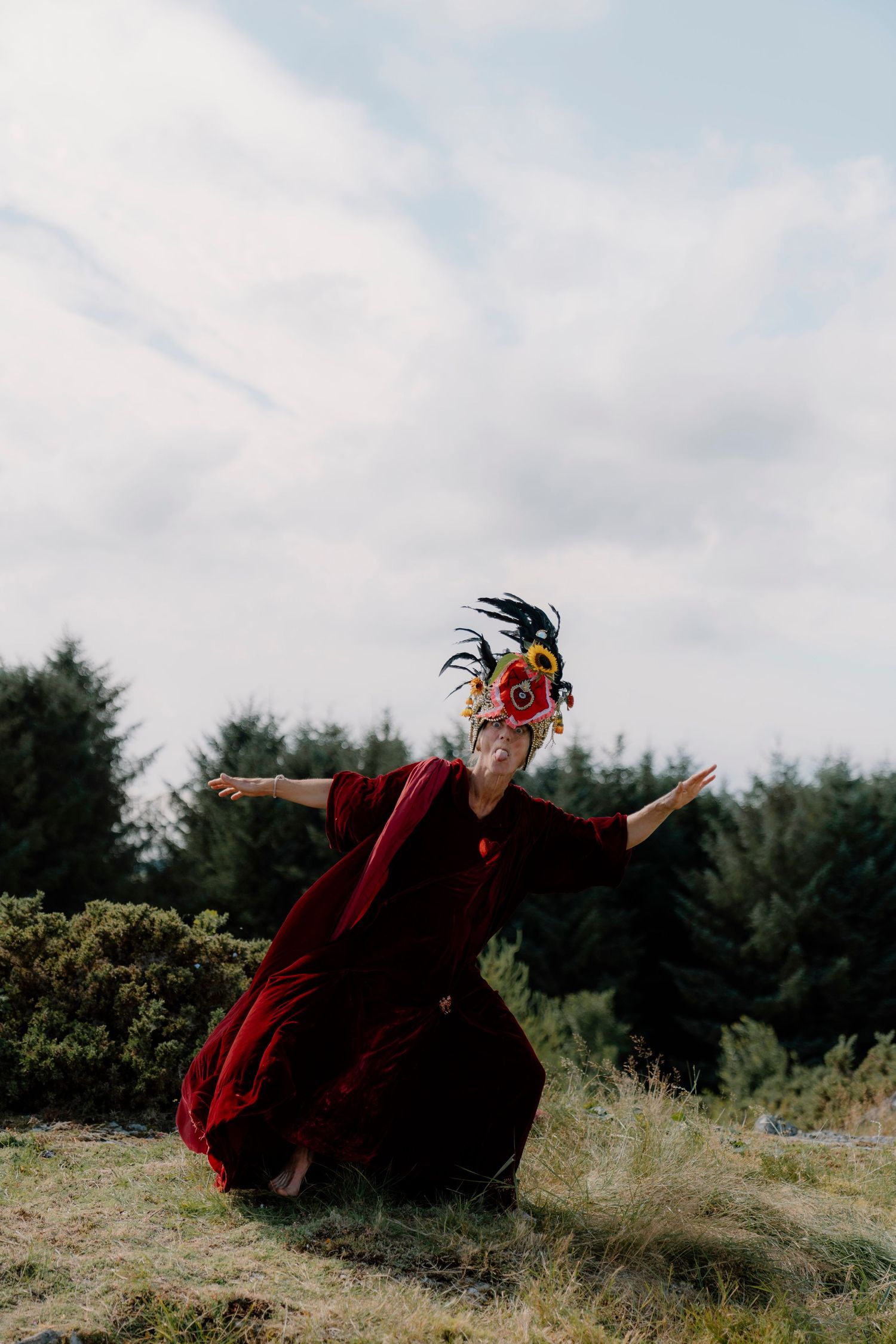 Person in flowing red dress and decorative mask poses dramatically outdoors.