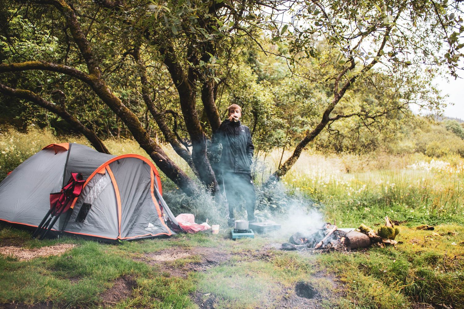 Campsite with tents set up in a wooded area showing multiple views of camping scenes with smoke rising from campfires.
