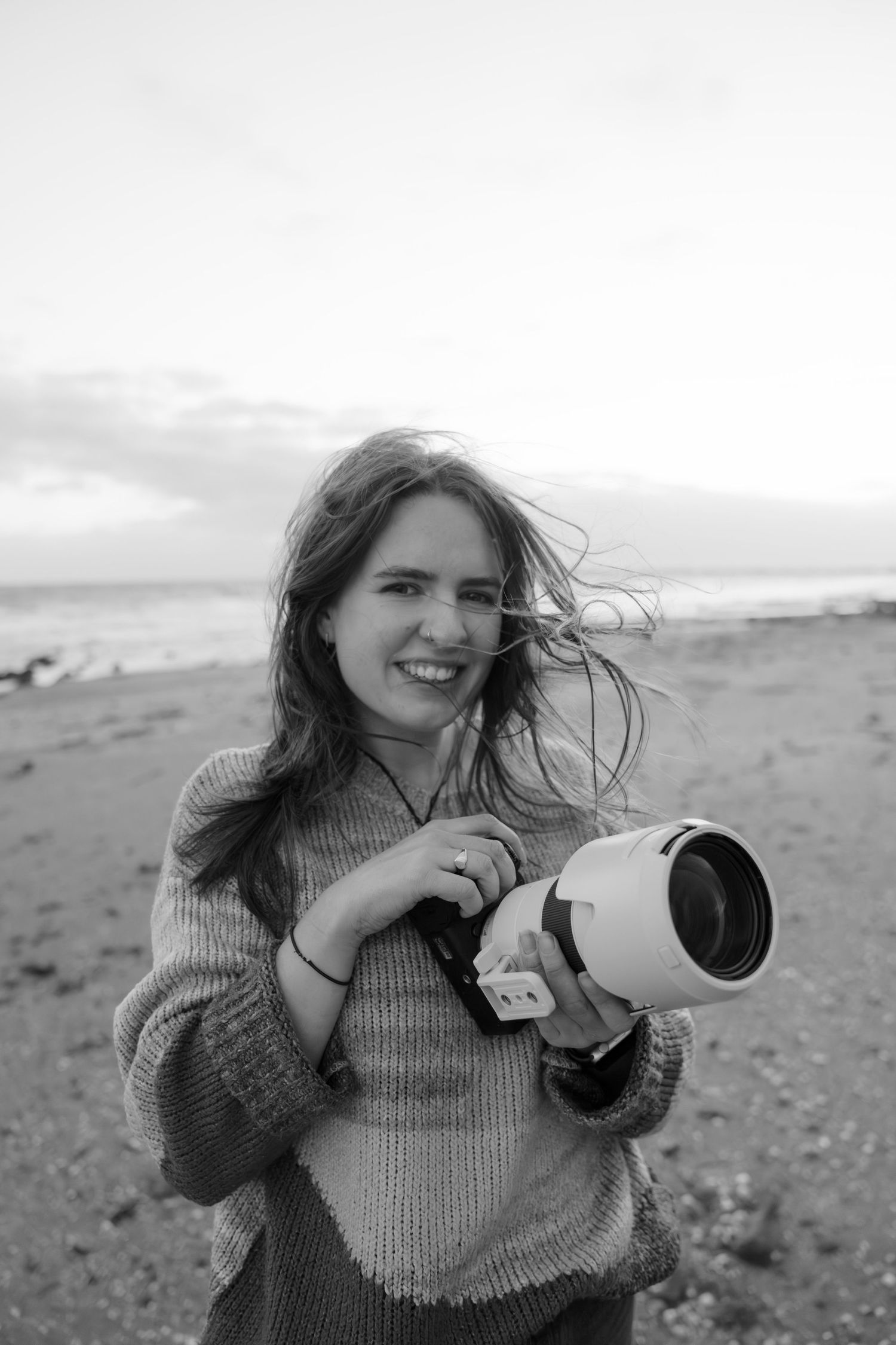 A person in a sweater drinks from a white mug in a series of four black and white photos on a beach.