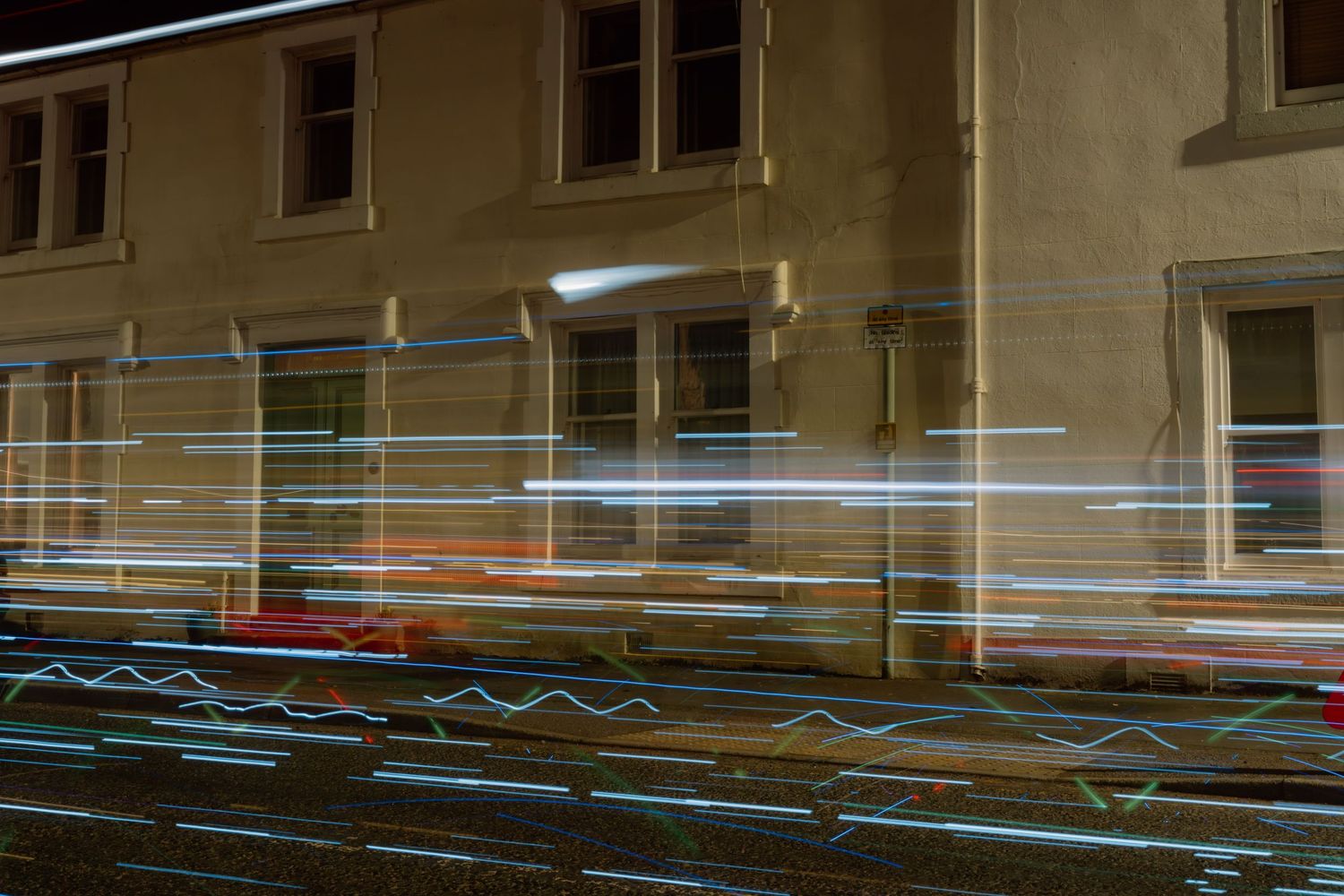 Long exposure night photography showing colorful light trails streaking past an old stone building.