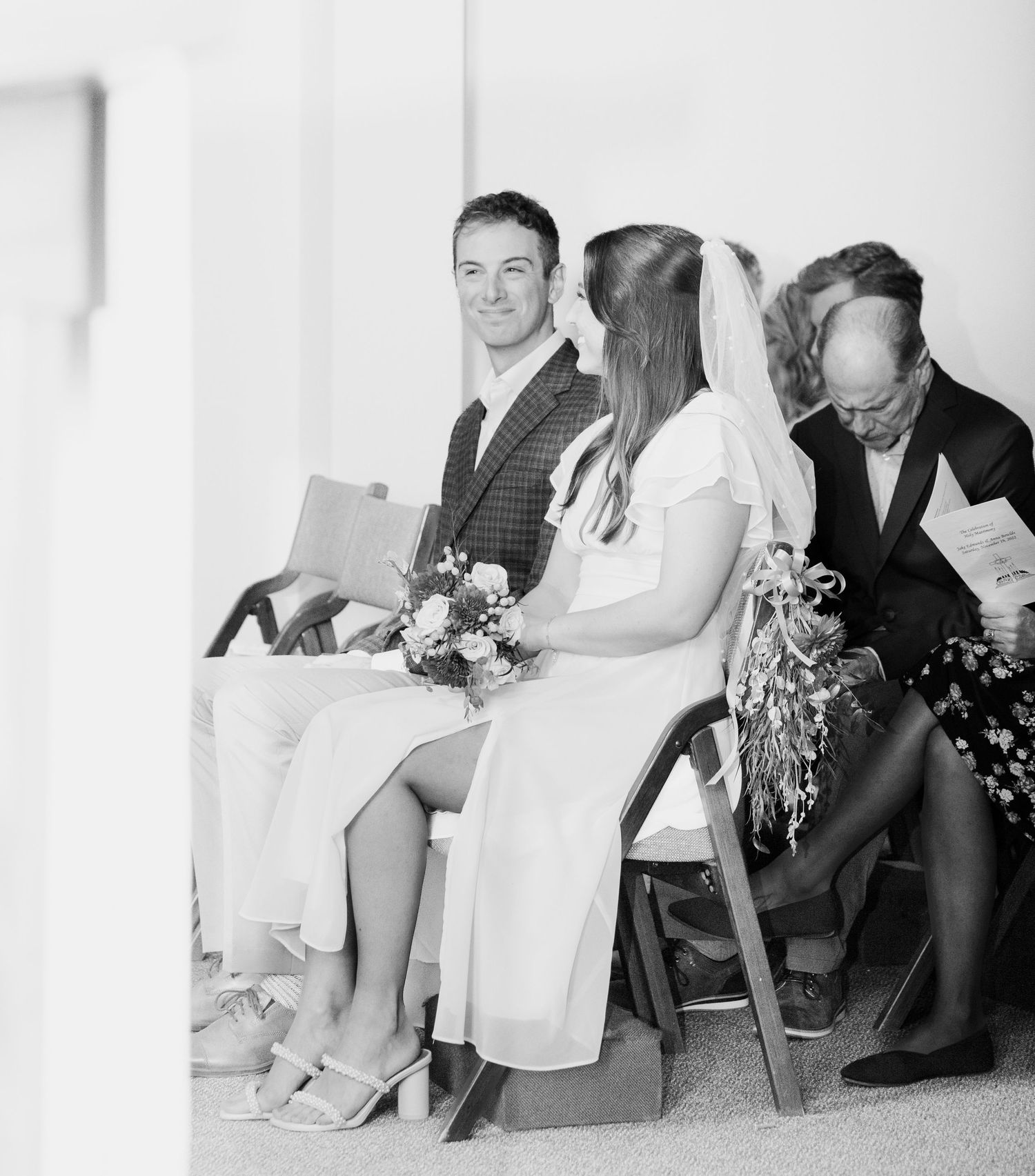A candid black and white photo of a wedding ceremony seating arrangement.