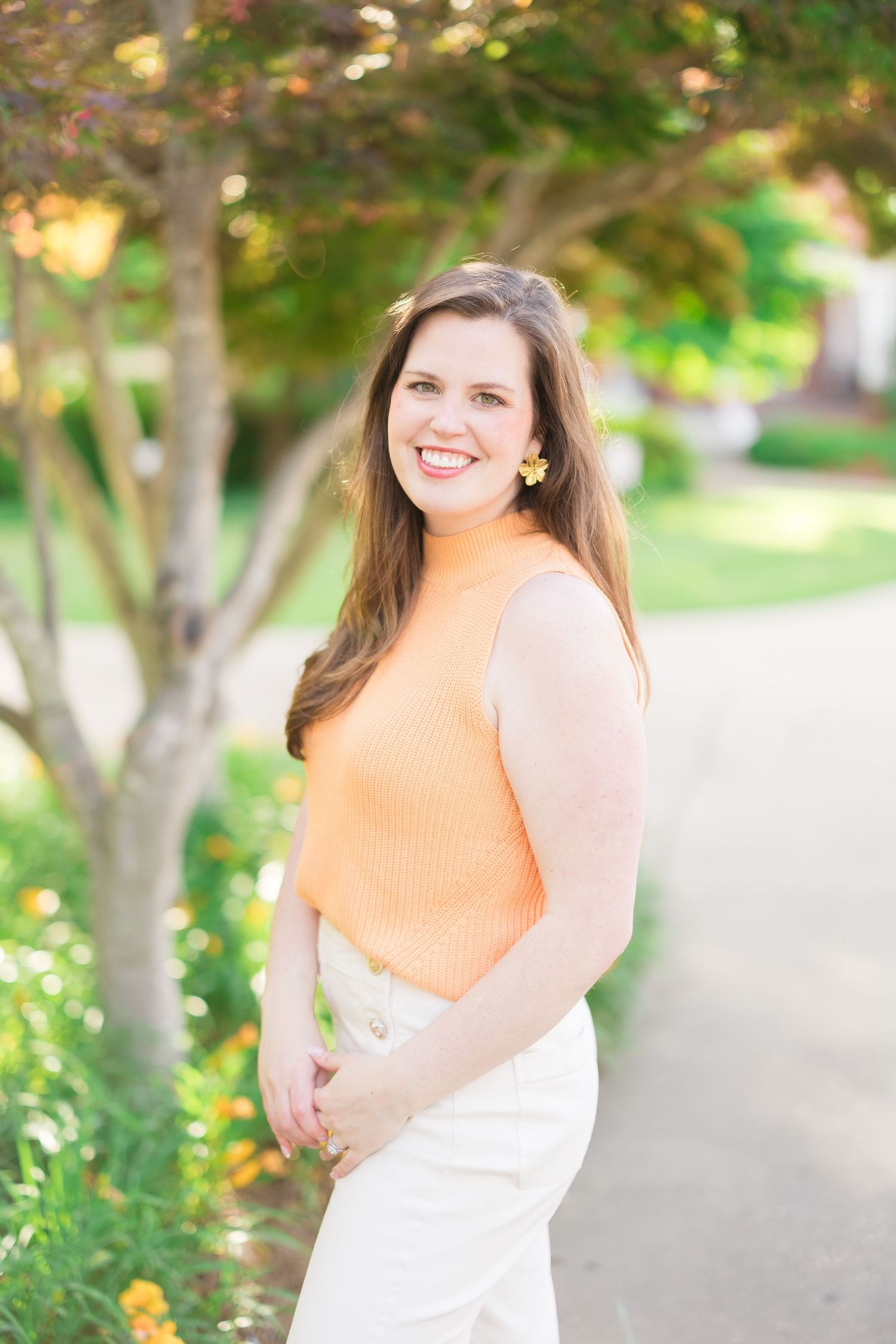 Woman in peach colored top poses outdoors in natural lighting.