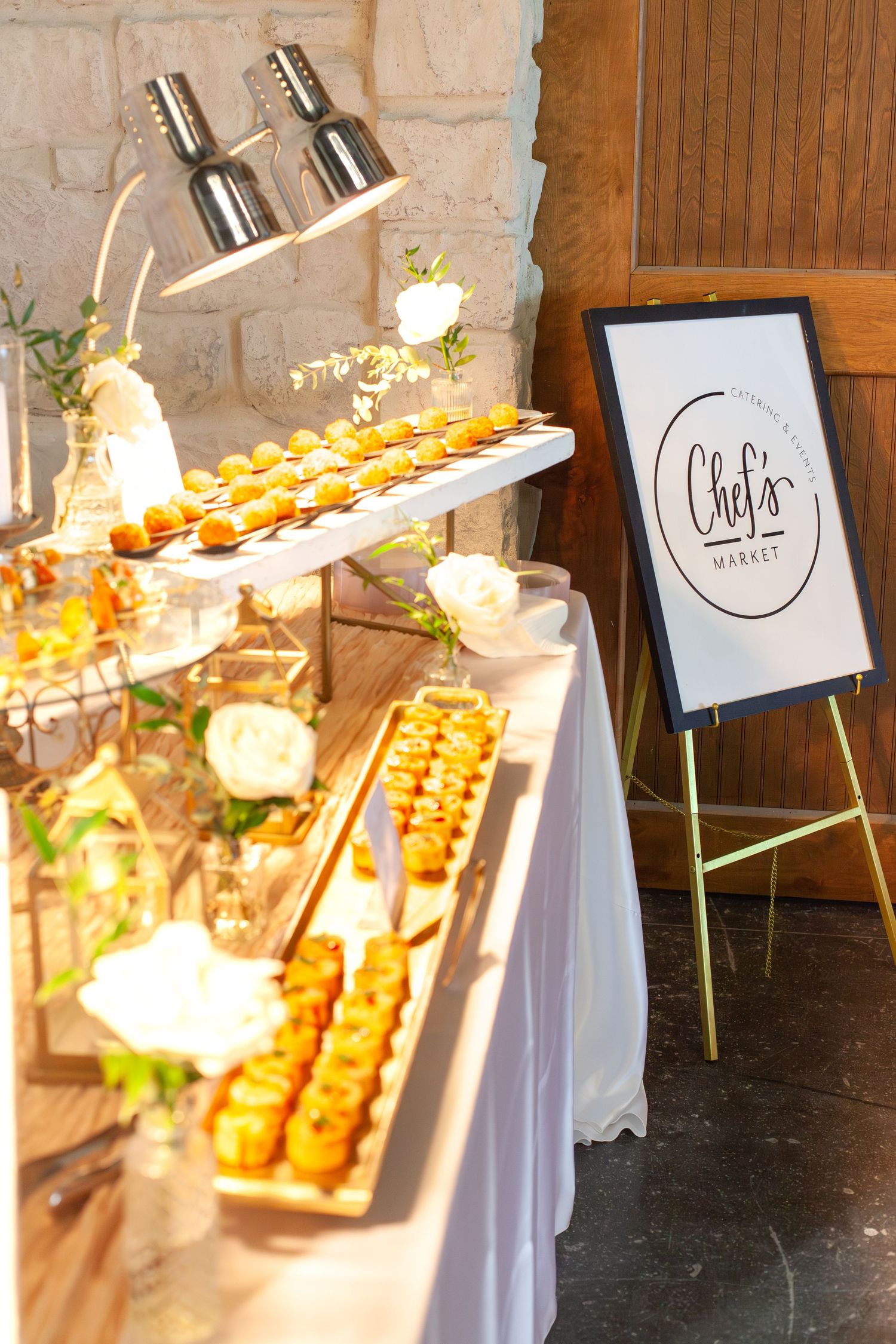Elegant Chef's Market catering display with tiered appetizers, warm lighting, and white floral arrangements at an upscale event.