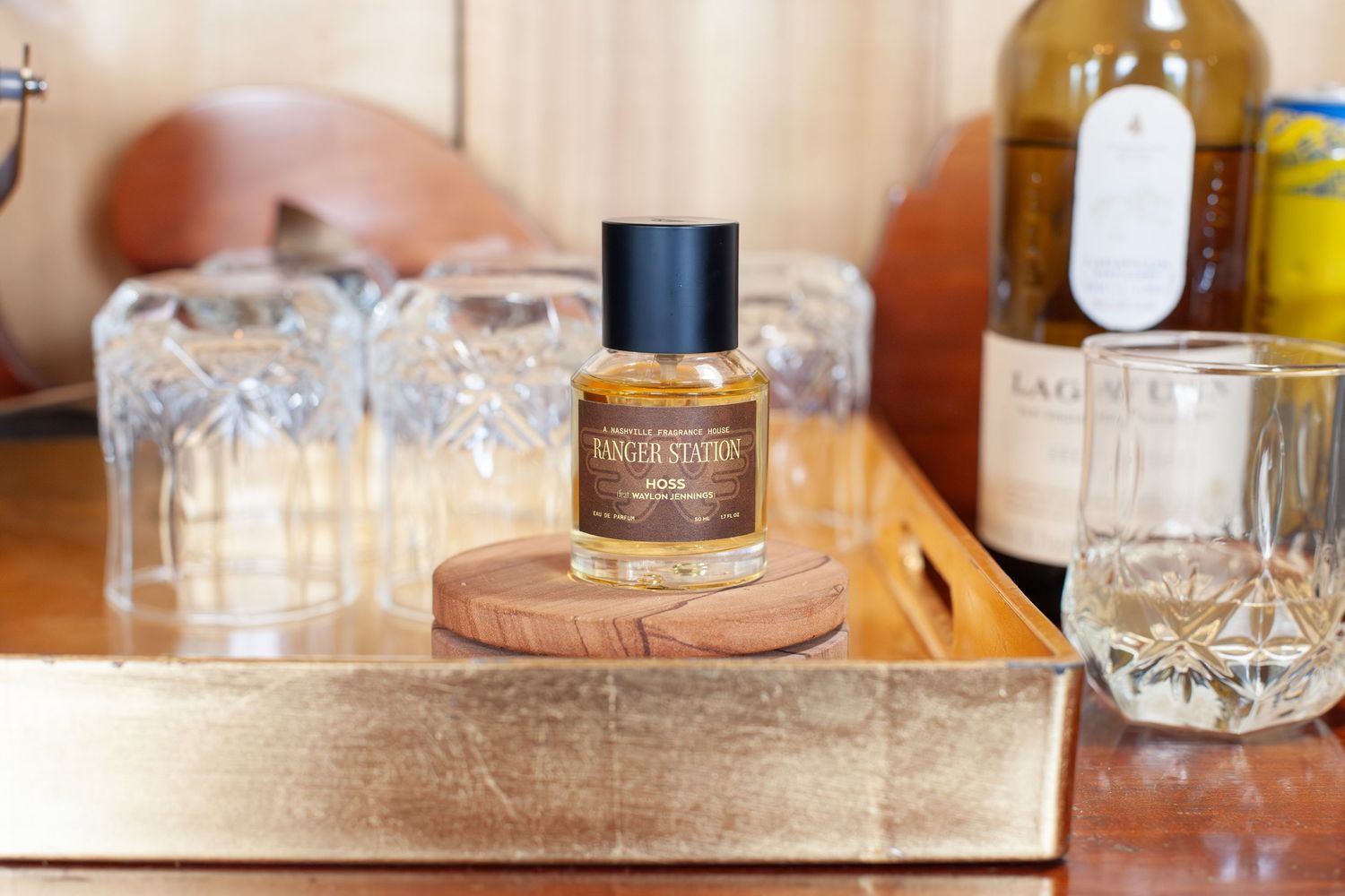 A luxury perfume bottle on a gold tray with crystal glasses and wine bottles in a stylish home bar setting.