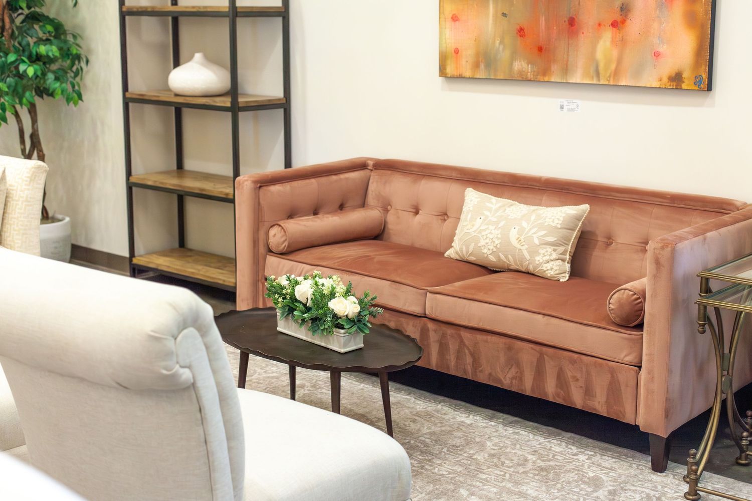 Elegant living room with a tufted velvet salmon sofa, white armchair, round coffee table, and colorful abstract wall art.