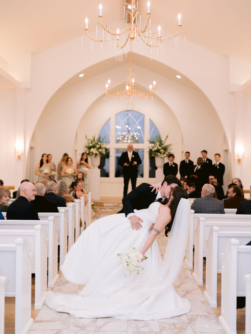 Beautiful white chapel interior with chandelier and arches during wedding ceremony.