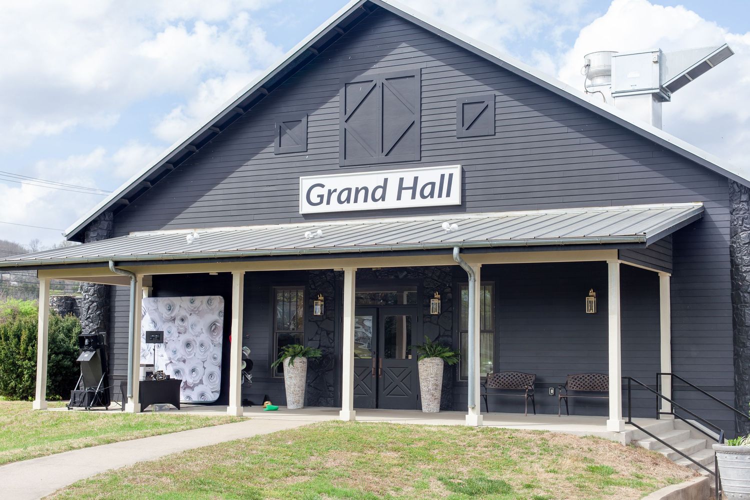 Exterior view of the Grand Hall event venue, a dark gray barn-style building with covered porch and signage.