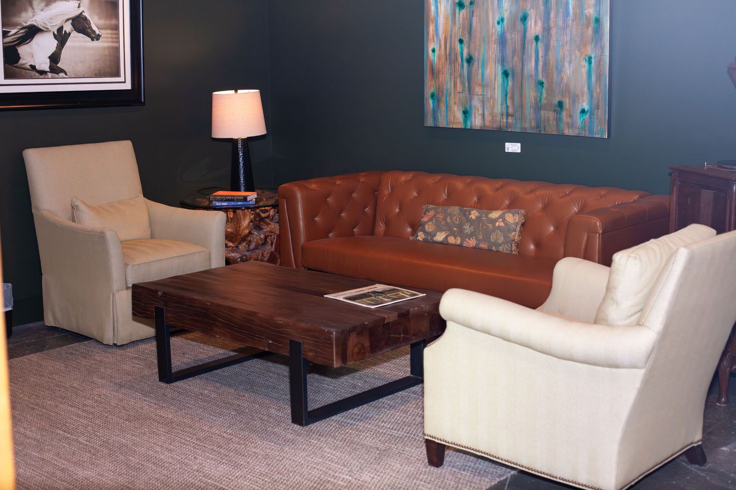 Modern living room with tufted leather sofa, white armchairs, wood coffee table, and colorful abstract wall art.