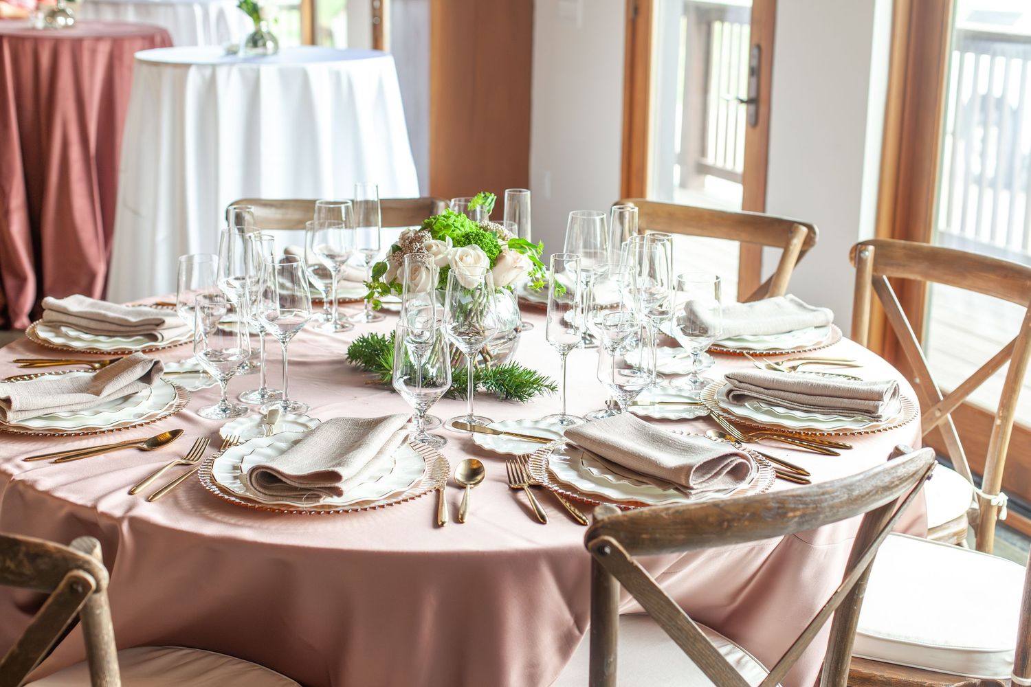 Elegant round wedding reception table with blush pink linen, crystal glassware, and floral centerpiece in a bright venue.