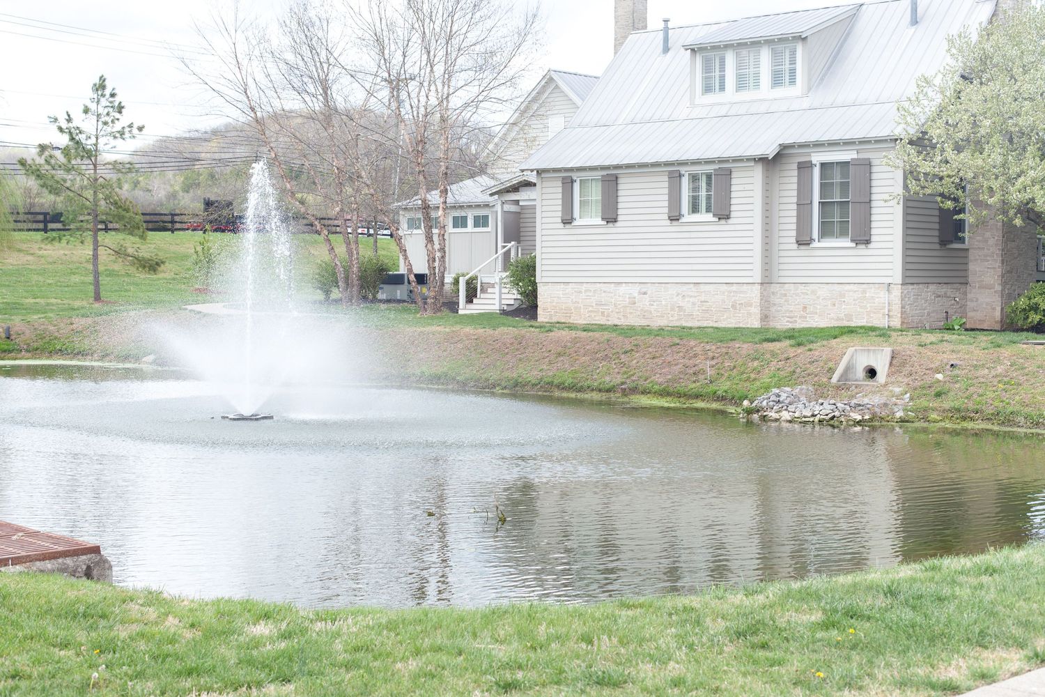Serene backyard pond with a water fountain feature, lush green lawn, and a charming residential home in the background.