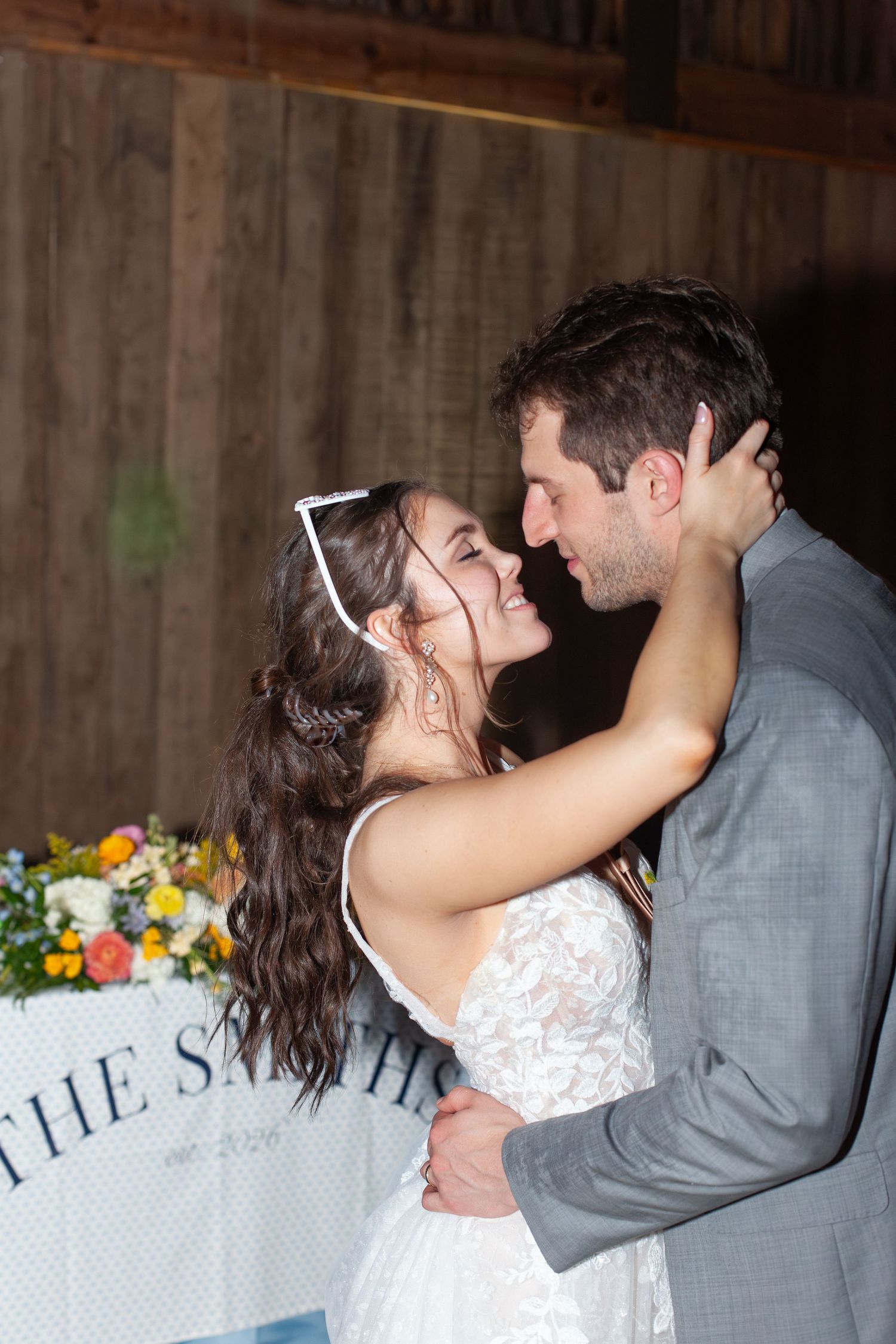 Bride and groom share a romantic embrace during their wedding reception in a rustic barn venue.