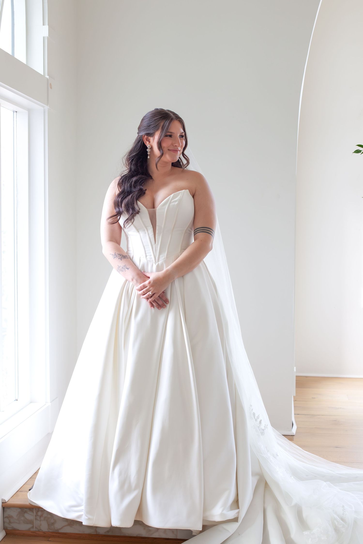Bride in strapless ivory satin ballgown wedding dress with sweetheart neckline and cathedral train in bright studio.