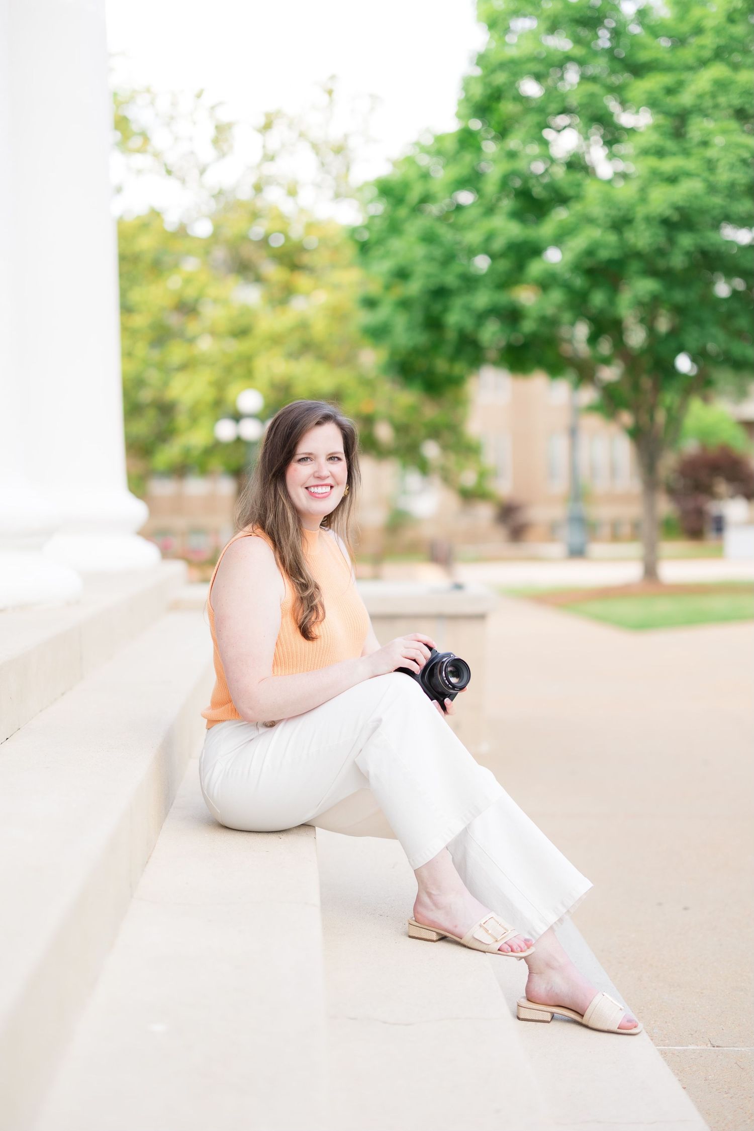 Woman in casual attire relaxing on white steps outdoors during a photo session.