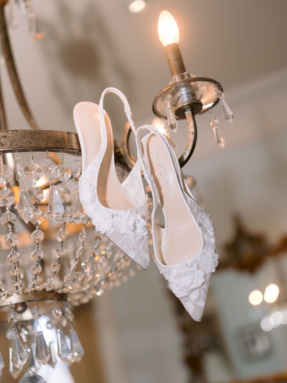 Vintage-style crystal chandelier adorned with white lace bridal shoes.