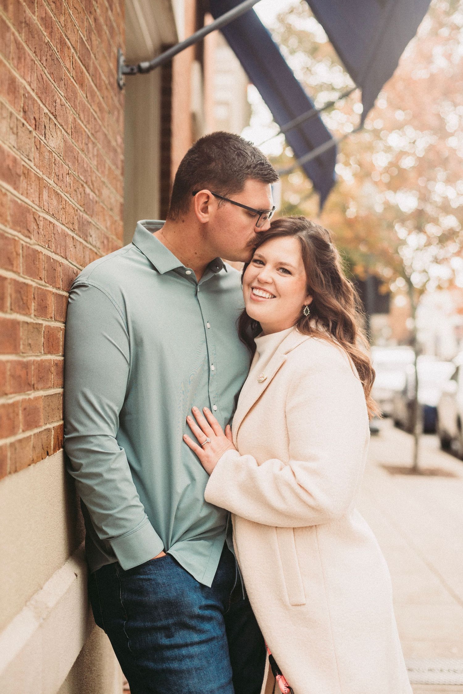 Couple shares intimate moment against brick wall during autumn engagement session.