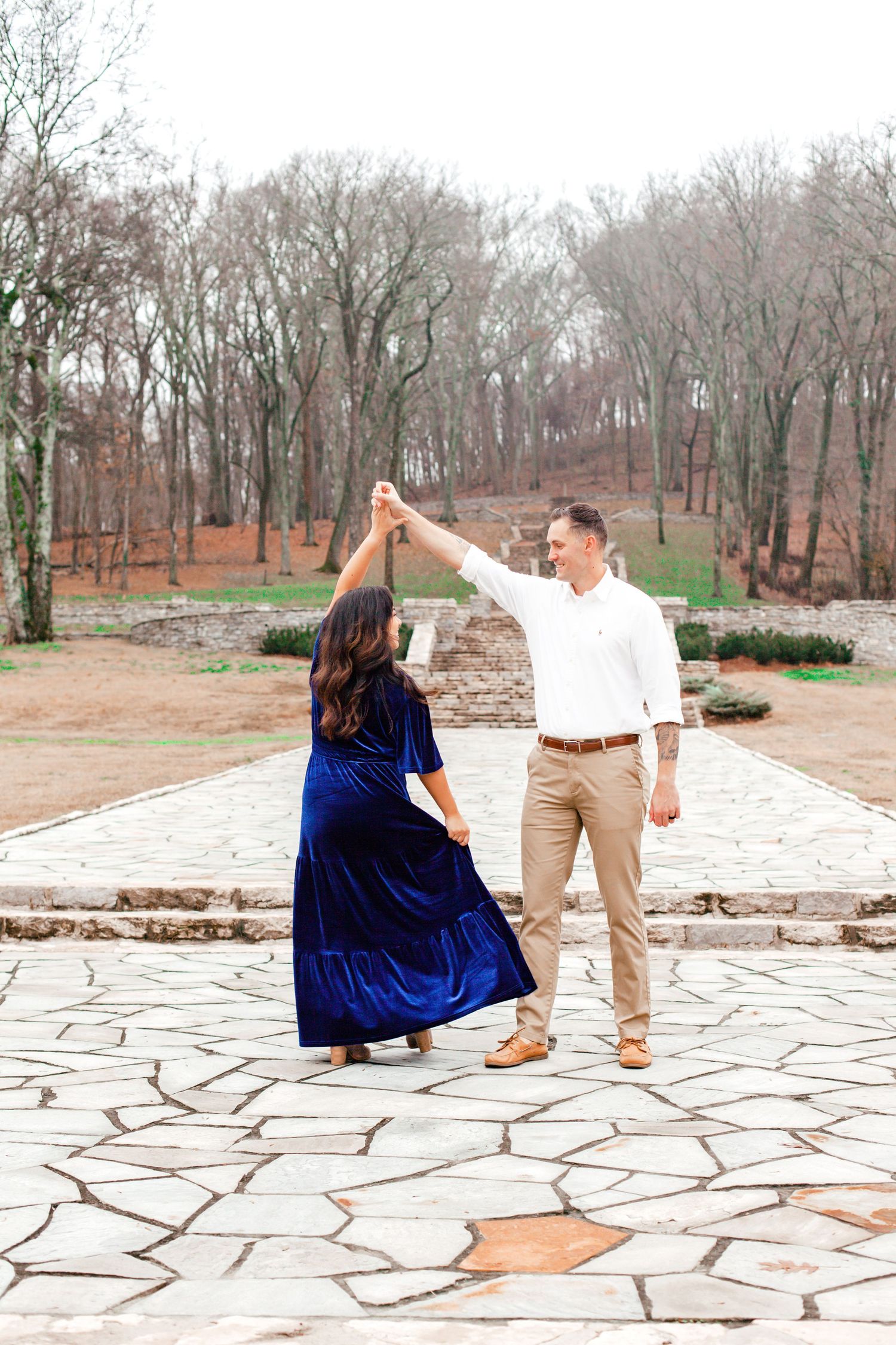 A couple poses together on a stone patio during a romantic outdoor photoshoot in a wooded setting.